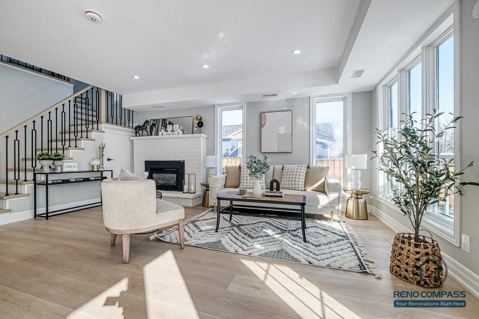This Georgian interior renovation features a bright living room with large windows, classic fireplace, elegant staircase railing, and light wood flooring. A refined and timeless interior completed by a professional Toronto renovation company.
