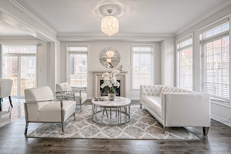 This Toronto modern luxury living room renovation showcases a bright and elegant interior with large windows, premium hardwood flooring, and sophisticated modern classic furnishings. The open layout highlights a custom fireplace feature wall, refined ceiling details, and high-end lighting that enhances the overall atmosphere. Completed by a professional Toronto renovation company, this residential interior project reflects timeless design, functional comfort, and upscale craftsmanship tailored for contemporary living.