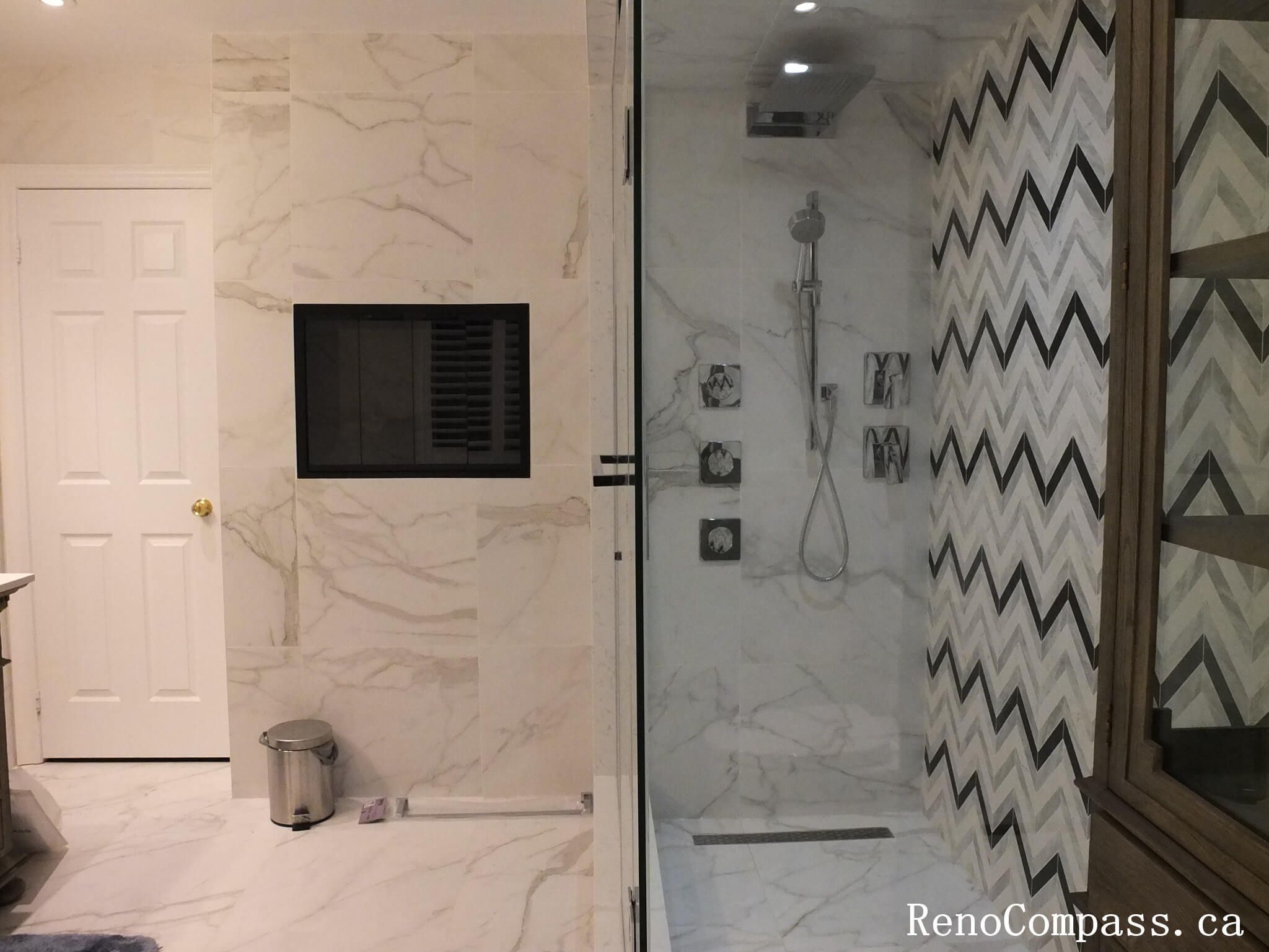 A wide view of a renovated bathroom in Markham featuring a glass-enclosed shower with chevron tiles and marble-patterned walls.