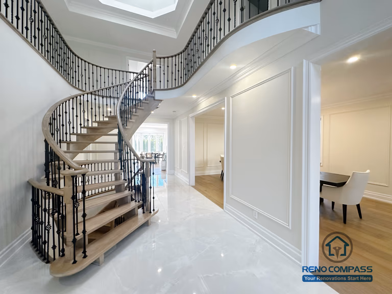This image showcases a flooring and stair renovation completed in North York, featuring a custom curved staircase with hardwood treads and decorative iron railings. The staircase serves as a central architectural element, enhancing flow and visual impact within the home. Surrounding flooring is finished with clean, light-toned surfaces that complement the staircase design and improve overall brightness. This renovation reflects a refined approach to flooring and stair upgrades, combining structural craftsmanship with elegant interior detailing for North York homes.