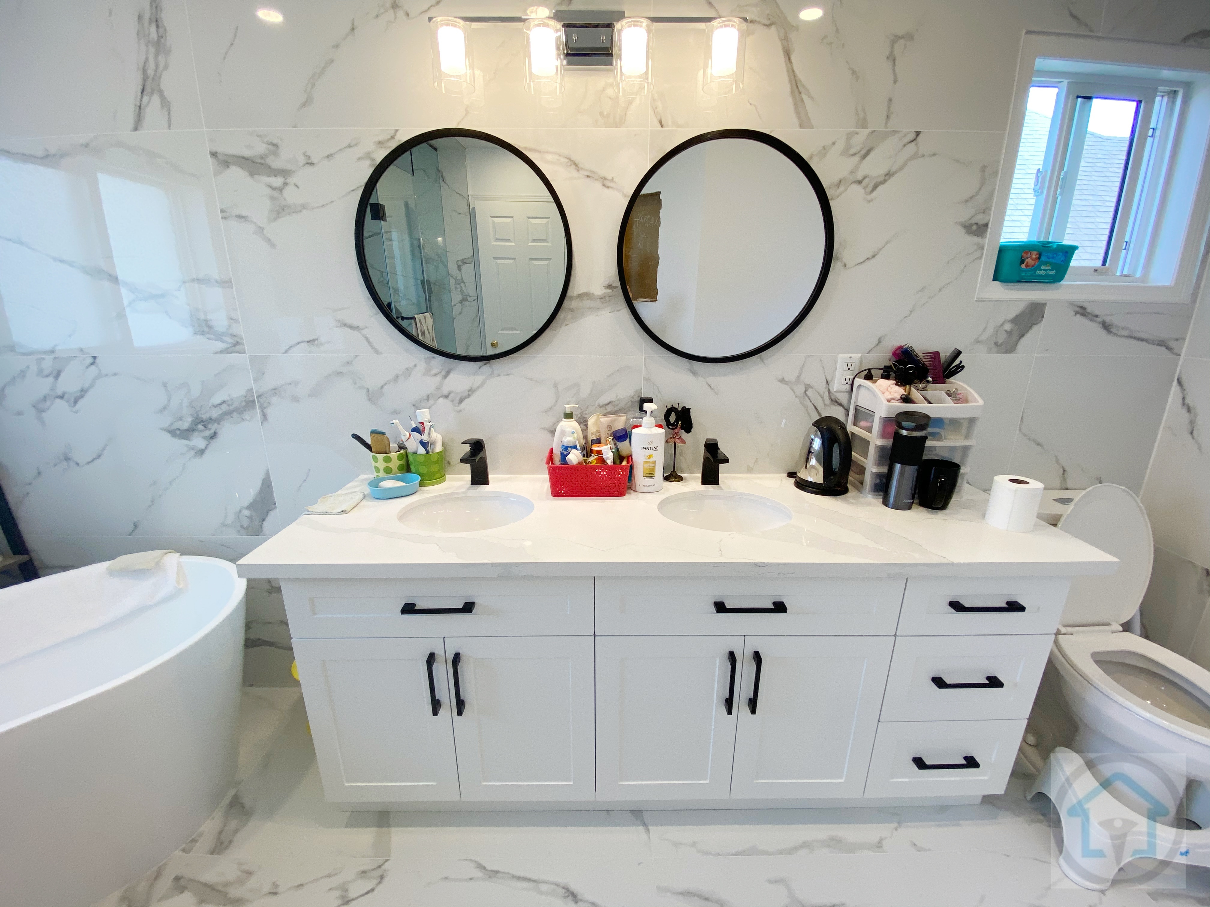 This Richmond Hill bathroom renovation features a custom double-sink vanity paired with round black-framed mirrors and modern wall-mounted lighting. The white shaker-style cabinetry is complemented by black hardware, creating a clean and balanced contrast against the marble-look wall tiles. Designed and completed by Reno Compass Inc., this bathroom remodel improves daily functionality while maintaining a timeless, easy-to-maintain aesthetic for Richmond Hill homes.