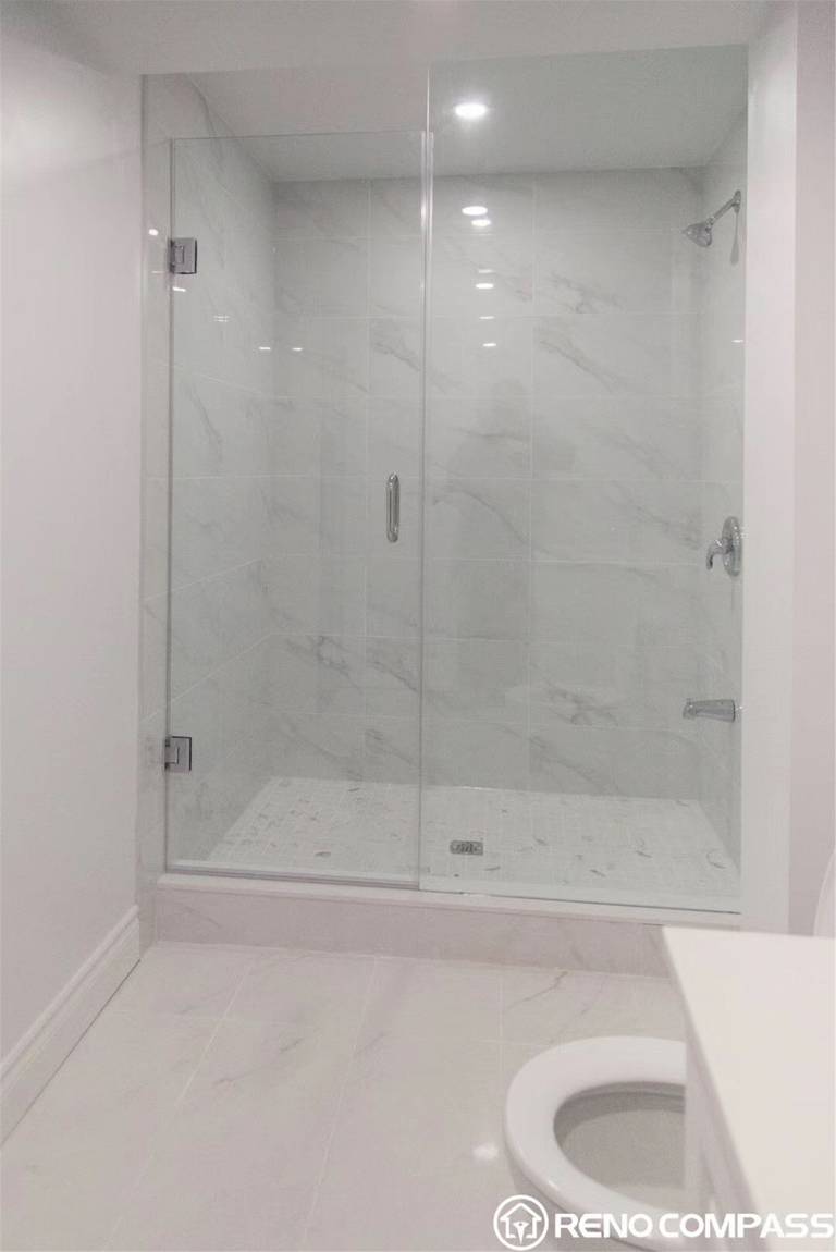 This Markham basement renovation showcases a modern bathroom upgrade featuring a frameless glass shower enclosure and marble-look wall tiles. The spacious walk-in shower is finished with large-format tiles, recessed lighting, and a clean, minimal design that enhances brightness and openness. The glass panel installation creates a seamless and contemporary appearance while maintaining functionality and durability. Completed by Reno Compass Inc., this basement bathroom renovation in Markham focuses on elegant finishes, efficient layout, and high-quality craftsmanship, transforming the lower level into a stylish and comfortable living space.