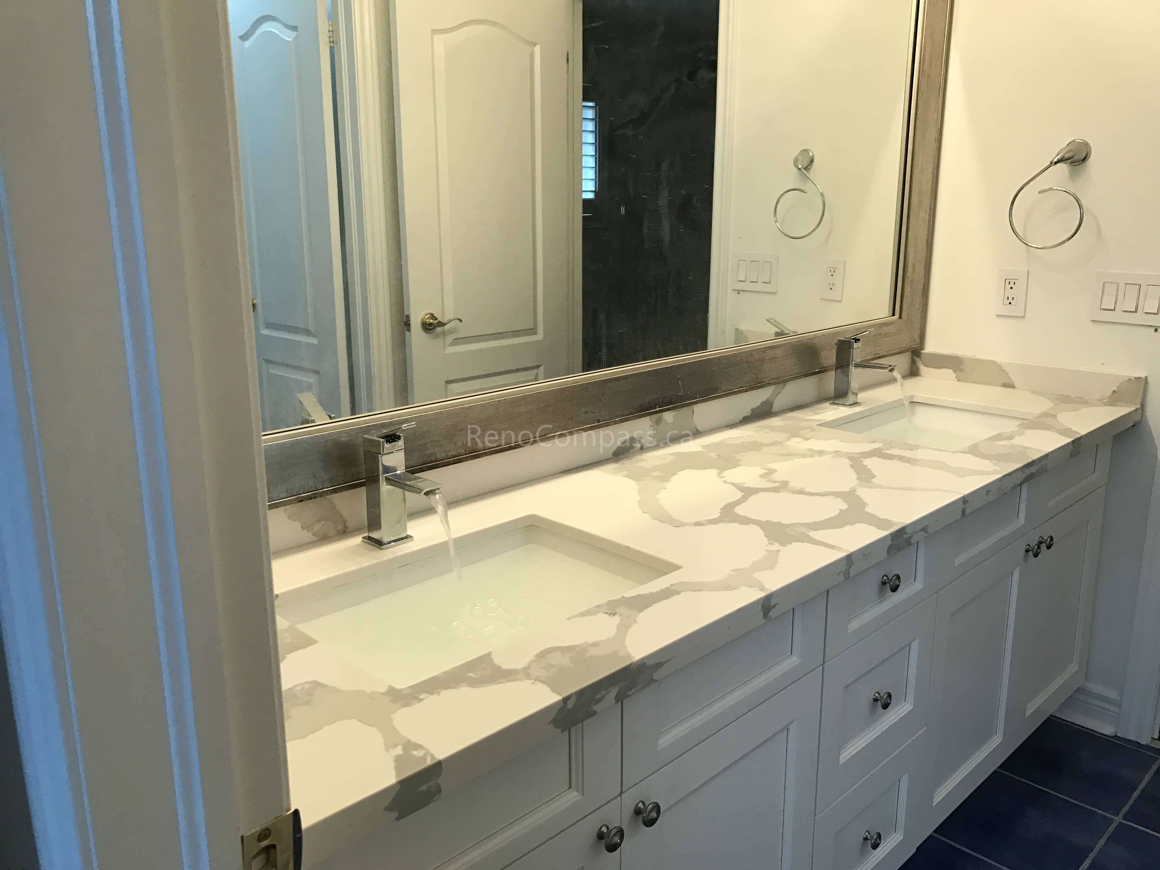 This Toronto bathroom renovation by Reno Compass features a custom double-sink vanity with a premium quartz countertop and modern square undermount sinks. The wide mirror and upgraded lighting enhance brightness and functionality, while the spacious cabinetry provides ample storage for everyday use. Designed with clean lines and durable materials, this elegant vanity upgrade adds both practicality and contemporary style to the bathroom space.