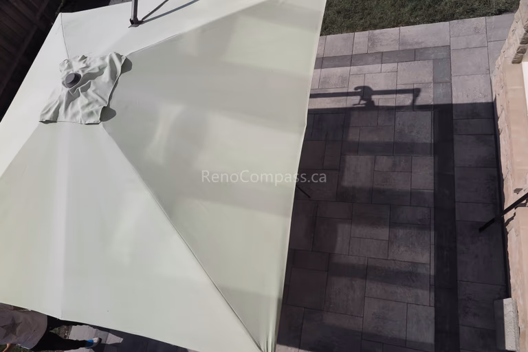 This Markham landscaping project showcases a detailed view of the professionally installed interlocking stone patio, designed with a modern geometric layout and contrasting border accents. The outdoor space is enhanced with a large patio umbrella, creating a comfortable shaded seating area for summer relaxation. Built using durable materials for long-term performance and minimal maintenance, this backyard upgrade reflects the quality workmanship of a trusted Toronto renovation company while elevating everyday outdoor living.