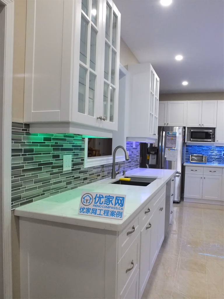 This Vaughan kitchen renovation highlights elegant white shaker cabinets with glass display doors, quartz countertops, and a modern glass mosaic backsplash enhanced by LED under-cabinet lighting. The clean layout and bright finishes create a stylish and functional cooking space. Completed by a trusted Toronto renovation company, the design blends modern aesthetics with everyday practicality.