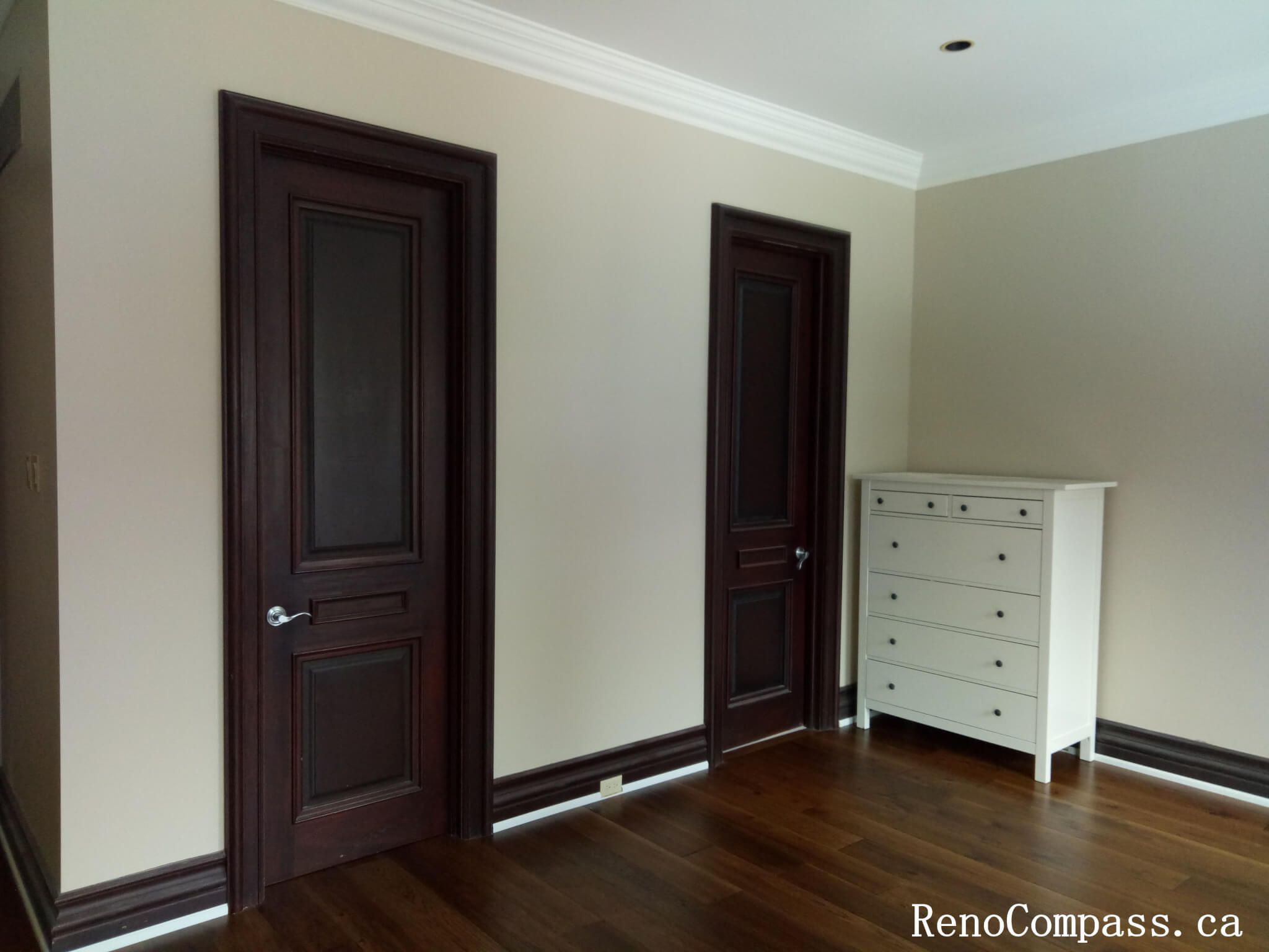 This image highlights a professionally completed interior painting project in North York, featuring smooth neutral wall finishes paired with crisp white crown molding and contrasting dark wood doors. Clean paint lines around door frames, baseboards, and ceiling details showcase precise workmanship and careful surface preparation. The balanced color palette enhances the warmth of the hardwood flooring while maintaining a timeless and elegant interior look. This North York painting project demonstrates attention to detail and high-quality finishes, suitable for bedrooms, hallways, or private living spaces.