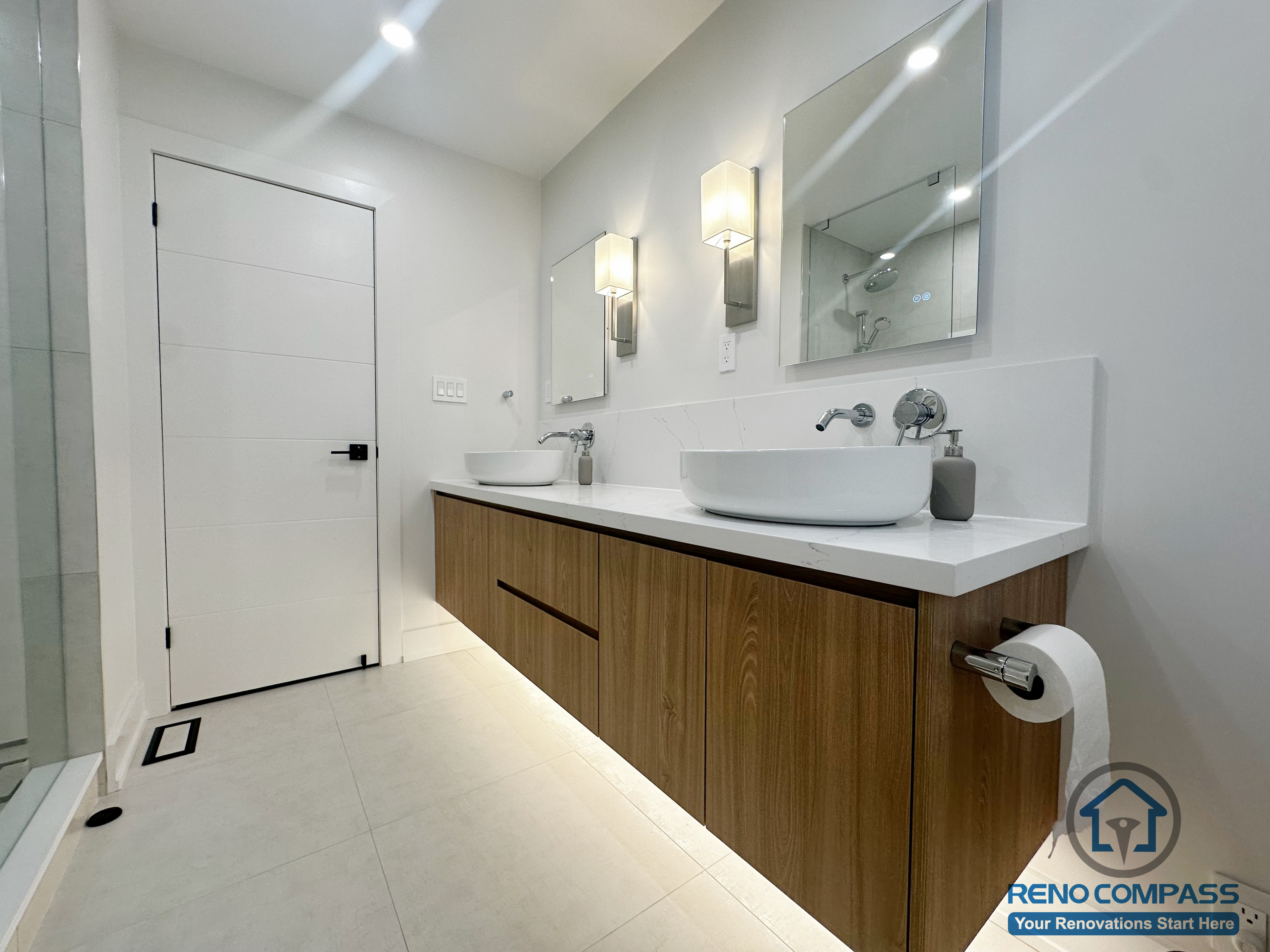 This Oakville bathroom renovation features a floating wood vanity paired with dual vessel sinks and a seamless quartz countertop. Integrated under-vanity lighting enhances the sense of space, while wall-mounted mirrors and modern sconces provide balanced, functional illumination. Clean-lined cabinetry and light porcelain flooring contribute to a refined, contemporary aesthetic designed for both daily use and long-term durability. Completed by Reno Compass, this bathroom reflects a modern approach to comfort and precision craftsmanship.