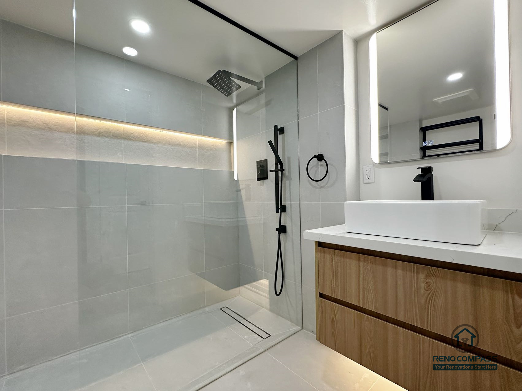 his completed bathroom renovation presents a cohesive curbless walk-in shower design paired with a floating wood vanity. Integrated niche lighting, large-format tiles, and a linear floor drain contribute to a clean and uninterrupted visual flow throughout the space. Matte black fixtures add contrast without overwhelming the neutral palette, while the vanity introduces warmth and balance. The overall layout is carefully planned to support efficient drainage, everyday comfort, and long-term usability.
Location: Pickering · Toronto Contractor: Reno Compass
