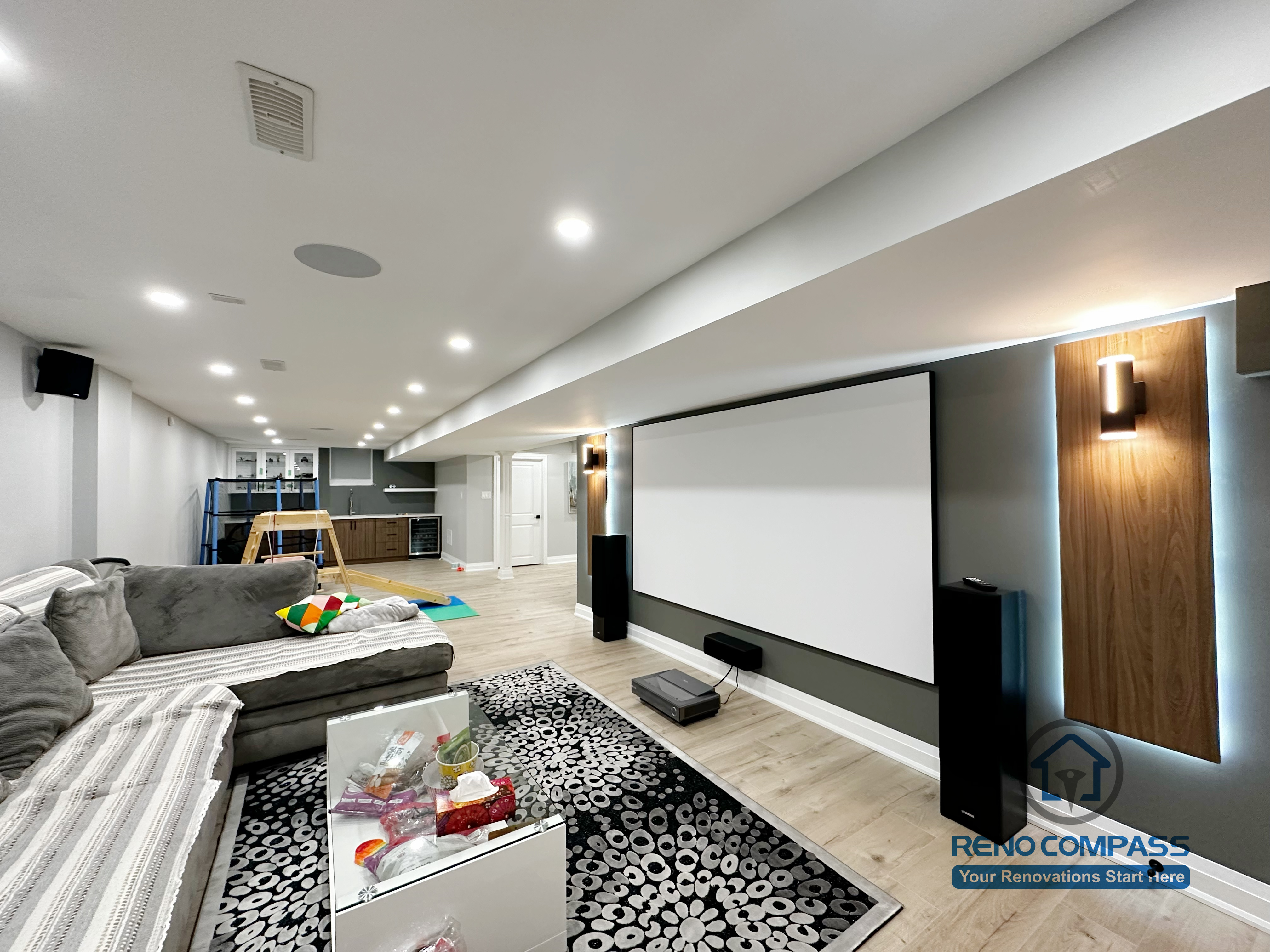 This modern Newmarket basement renovation features a custom home theater setup with a built-in projector screen, recessed ceiling lighting, and a clean, contemporary layout. The finished basement combines entertainment and family living, showcasing professional lighting design, smooth ceiling work, and warm flooring for a comfortable and functional space.