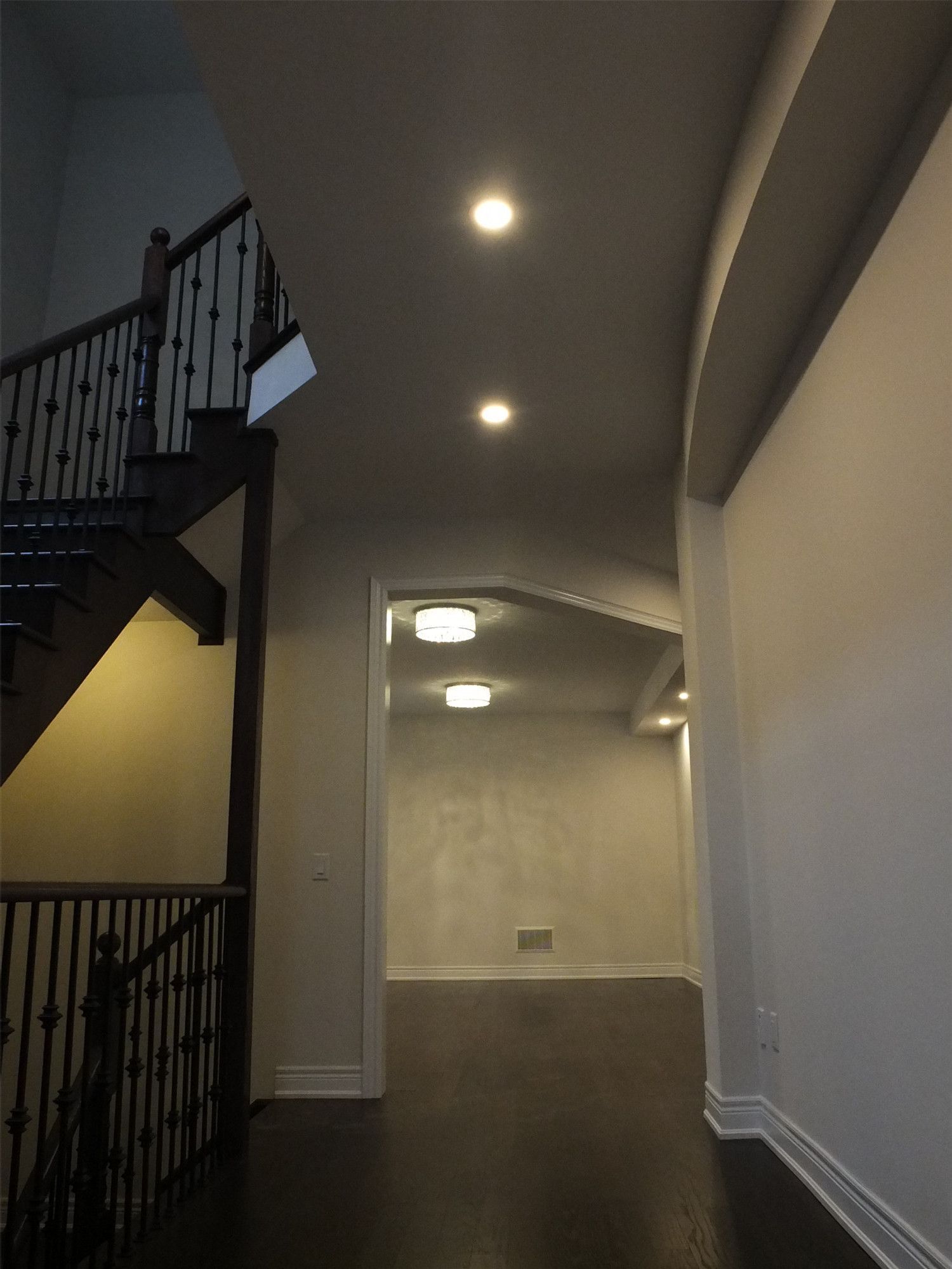 This Kleinburg interior renovation features a refined hallway and staircase area with dark hardwood flooring and modern recessed pot lighting. The staircase with black railings adds architectural character, while the soft ceiling lighting provides a warm and inviting atmosphere throughout the corridor. Clean wall finishes and balanced lighting enhance the spacious feel of the interior, creating a polished and contemporary residential design.