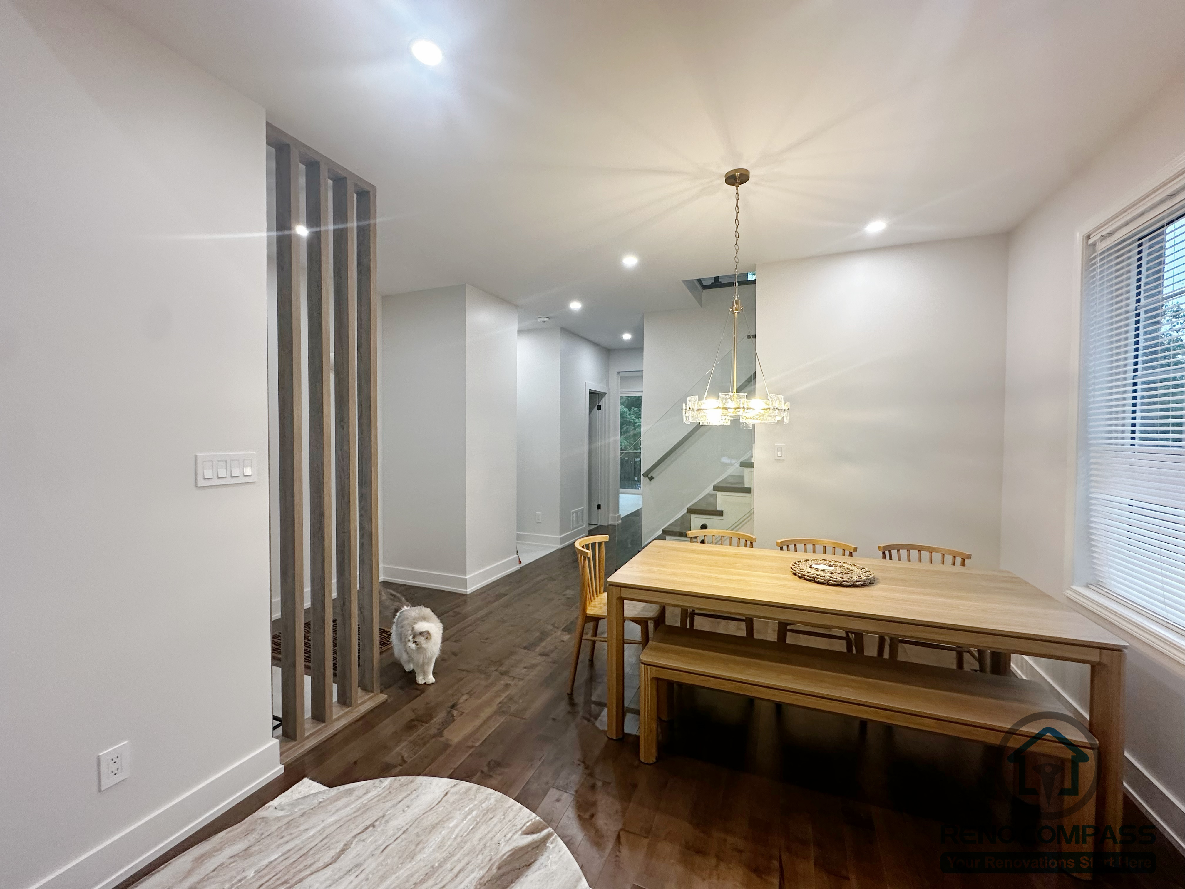 This Oakville dining area renovation emphasizes open sightlines and smooth circulation between shared living spaces. Wood flooring runs continuously through the dining zone and hallway, creating visual continuity throughout the main floor. A simple pendant light anchors the dining table, while vertical slat detailing adds subtle separation without closing off the space. The layout supports both daily family use and flexible entertaining.