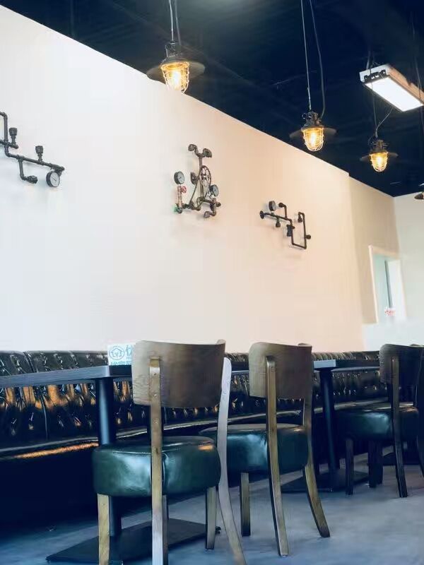This image showcases a finished dining area within a cafeteria commercial renovation project in North York. The space features a row of custom seating paired with wooden chairs, a clean white feature wall, and decorative wall-mounted elements that add character without overwhelming the space. Pendant lighting and an open ceiling design contribute to a modern, inviting atmosphere suitable for casual dining and social interaction. This North York cafeteria commercial renovation highlights thoughtful layout planning, durable furniture selection, and cohesive interior styling by a Toronto renovation company specializing in commercial hospitality spaces.