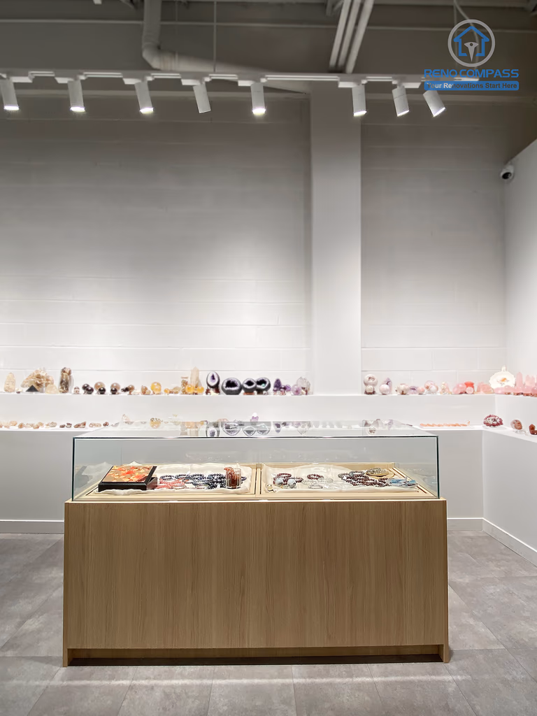 This image presents the central display area of a crystal shop renovation in Markham, featuring a custom-built wood and glass display island positioned along the main visual axis of the store. Wall-mounted crystal shelves, polished concrete flooring, and professional track lighting work together to create a clean, balanced, and gallery-like retail environment. The symmetrical layout enhances product visibility and customer flow. As a Toronto renovation company, Reno Compass specializes in retail renovations that combine thoughtful space planning with refined visual presentation.