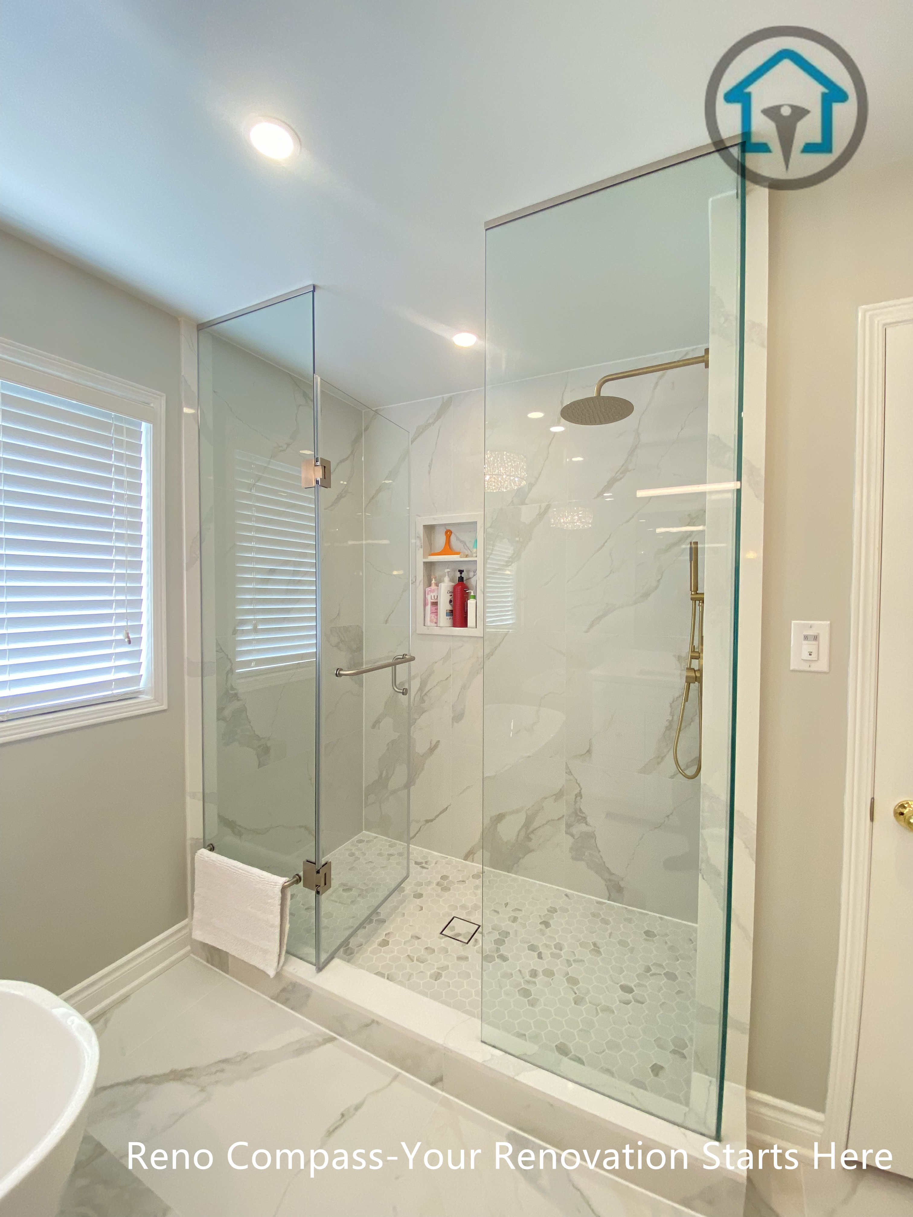 This Mississauga bathroom renovation features a spacious walk-in shower enclosed with frameless clear glass panels to enhance openness and natural light. Large-format marble-look wall tiles are paired with a mosaic tile shower floor for slip resistance and visual contrast. Gold-tone shower fixtures add warmth and elegance, while a built-in wall niche provides functional storage without disrupting the clean layout. The shower design prioritizes comfort, drainage efficiency, and long-term durability through precise detailing and quality materials.