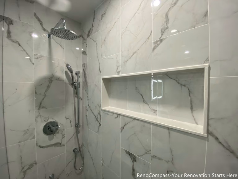 This Oakville bathroom renovation features a modern walk-in shower with large-format marble-look tiles, a built-in recessed shower niche, and a sleek rainfall shower system. The clean tile layout and contemporary fixtures create a bright, spa-inspired shower space that combines style with practicality. Completed by a trusted Toronto renovation company, this upgrade focuses on waterproofing quality, durable materials, and functional storage solutions to deliver a modern bathroom designed for comfort and long-term performance.