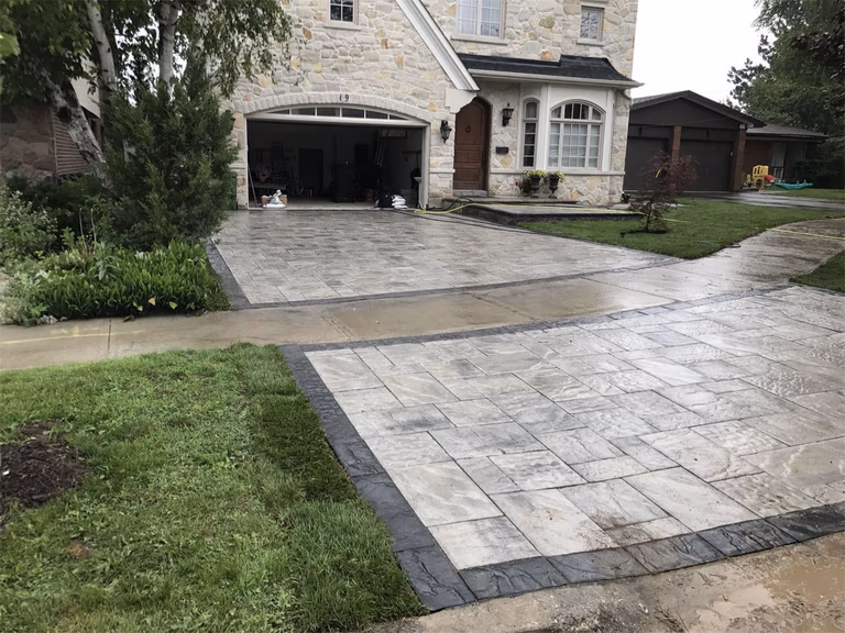 Residential landscaping renovation in Toronto featuring a large interlocking driveway and connecting walkway with decorative borders. The design enhances curb appeal while providing a durable and visually balanced front yard entrance.