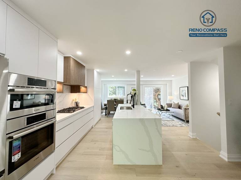 This Richmond Hill interior renovation features a bright open-concept kitchen and living space with custom white cabinetry, integrated stainless steel appliances, a waterfall kitchen island, and wide-plank hardwood flooring. Designed and completed by a Toronto renovation company, the layout enhances natural light, functionality, and modern living comfort for contemporary family homes.