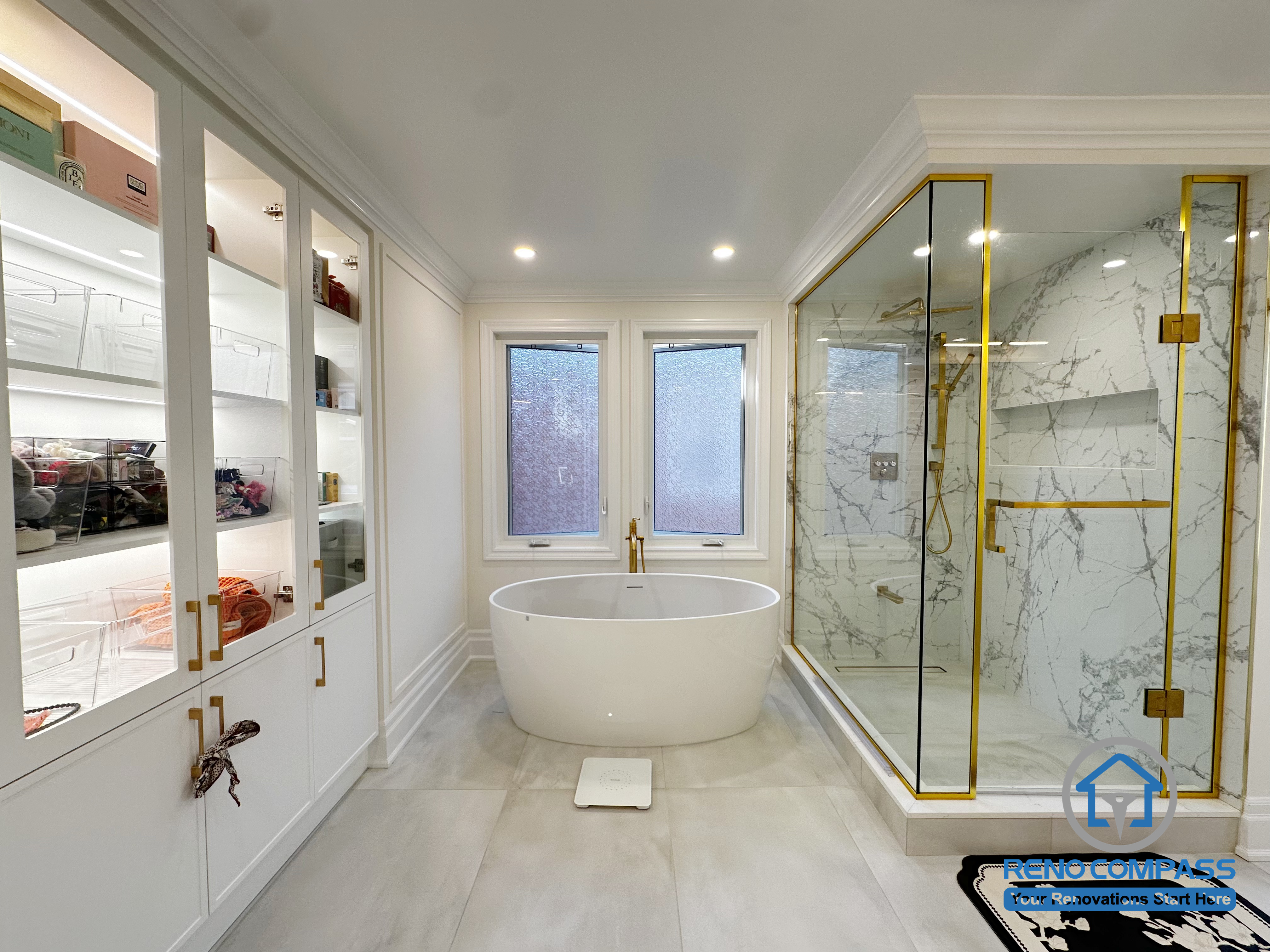This Markham bathroom renovation features a balanced layout that combines a freestanding bathtub, a frameless glass shower, and custom built-in storage. The space is designed to feel open and refined, with light-toned surfaces, elegant trim details, and glass cabinetry that adds both display and organization. Gold-accent finishes and natural light enhance the sense of luxury while maintaining a calm, timeless atmosphere. The result is a well-composed bathroom that prioritizes comfort, functionality, and visual harmony.