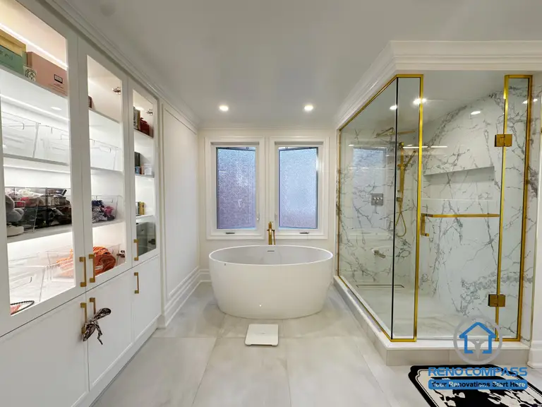 This Markham bathroom renovation features a balanced layout that combines a freestanding bathtub, a frameless glass shower, and custom built-in storage. The space is designed to feel open and refined, with light-toned surfaces, elegant trim details, and glass cabinetry that adds both display and organization. Gold-accent finishes and natural light enhance the sense of luxury while maintaining a calm, timeless atmosphere. The result is a well-composed bathroom that prioritizes comfort, functionality, and visual harmony.