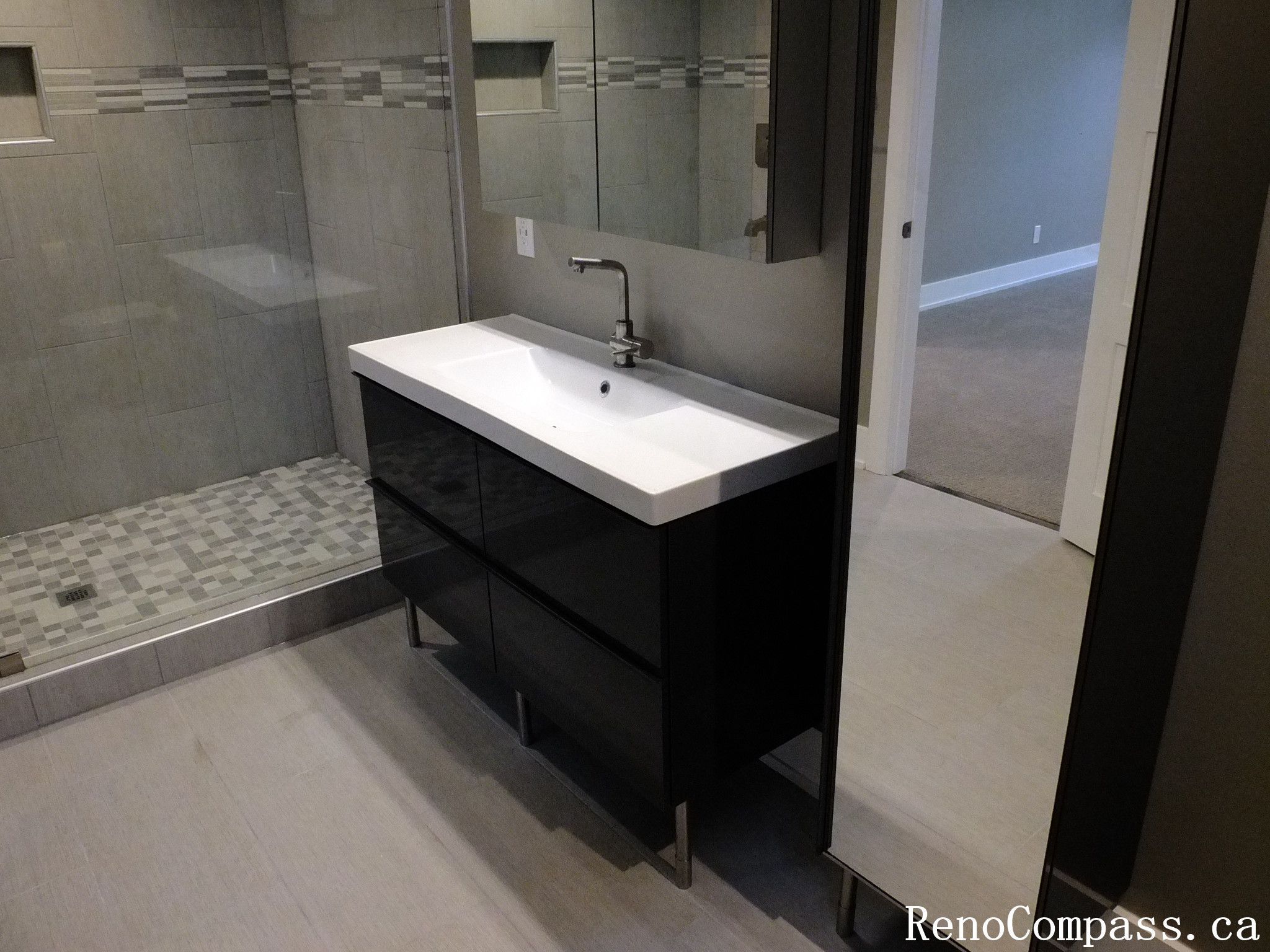 Stylish basement bathroom renovation in Waterloo featuring a sleek floating vanity, large mirror, modern fixtures, and a custom tile shower with mosaic floor and frameless glass enclosure. A clean, contemporary upgrade to the lower level.