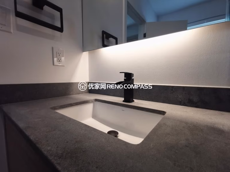 Bathroom sink detail from a North York interior renovation, featuring an integrated rectangular sink, stone countertop, and matte black faucet. The wall-mounted mirror with built-in LED lighting provides even illumination while maintaining a clean, minimalist appearance. Neutral material tones and concealed detailing enhance durability and ease of maintenance, reflecting a modern bathroom renovation completed by a Toronto renovation company focused on precision and functional design.