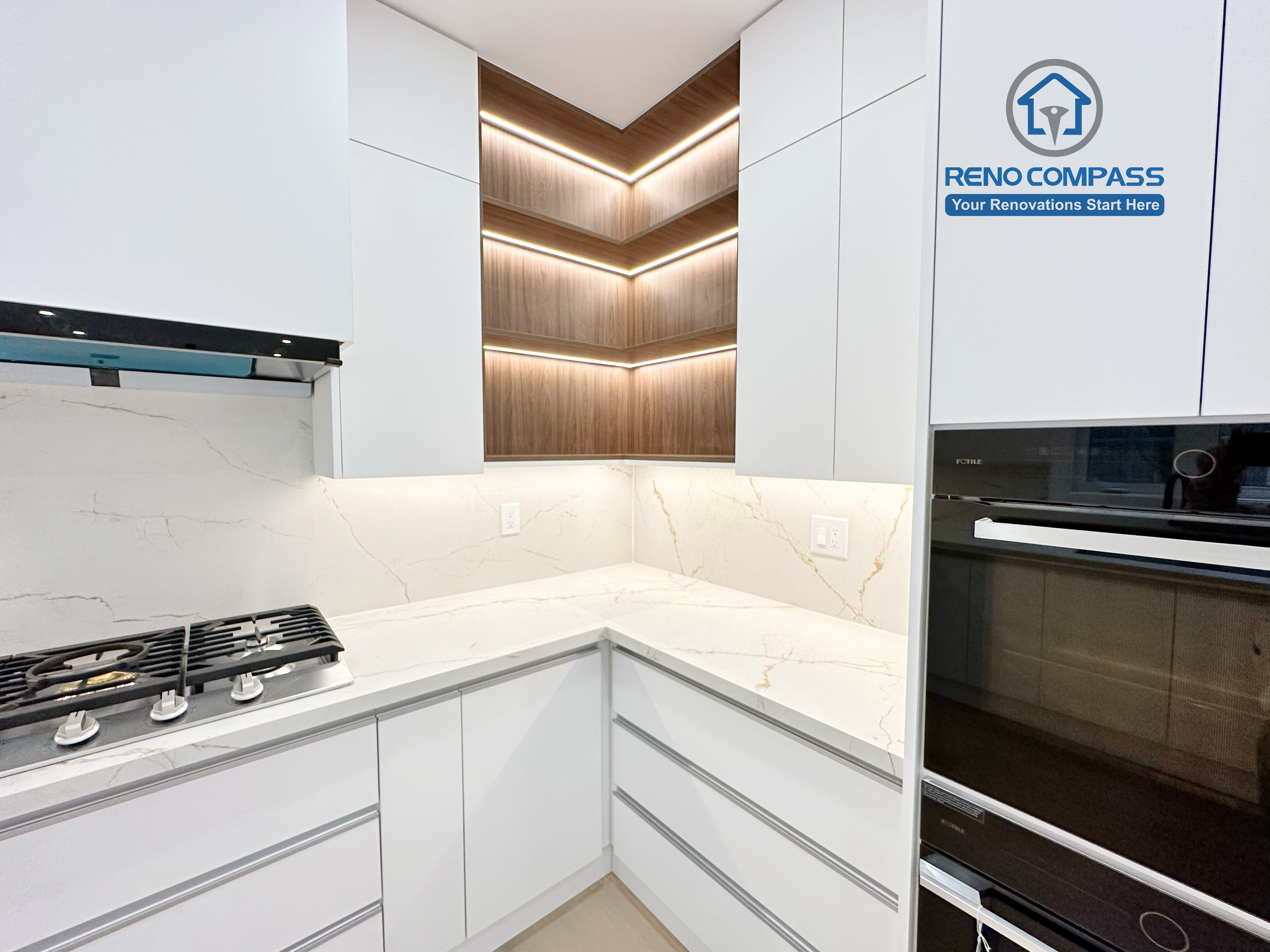 This image captures a detailed view of a modern kitchen renovation in Richmond Hill, highlighting custom corner cabinetry with integrated LED accent lighting. The design features seamless white handle-less cabinets, warm wood shelving with built-in lighting, quartz countertops, and a marble-look backsplash. A built-in gas cooktop and integrated wall oven enhance both functionality and aesthetics. Completed by an experienced Toronto Renovation Company, this kitchen renovation demonstrates refined craftsmanship, smart storage solutions, and contemporary lighting design.