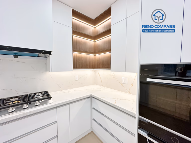 This image captures a detailed view of a modern kitchen renovation in Richmond Hill, highlighting custom corner cabinetry with integrated LED accent lighting. The design features seamless white handle-less cabinets, warm wood shelving with built-in lighting, quartz countertops, and a marble-look backsplash. A built-in gas cooktop and integrated wall oven enhance both functionality and aesthetics. Completed by an experienced Toronto Renovation Company, this kitchen renovation demonstrates refined craftsmanship, smart storage solutions, and contemporary lighting design.