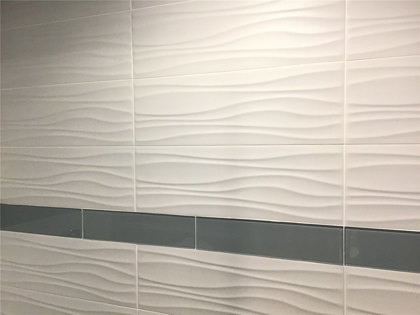 This Richmond Hill basement renovation features a modern bathroom wall design using textured 3D wave tiles combined with a sleek horizontal accent strip. The neutral color palette enhances the space with a clean and contemporary look, making it ideal for functional and stylish basement bathrooms. Perfect example of high-quality basement finishing in Richmond Hill.