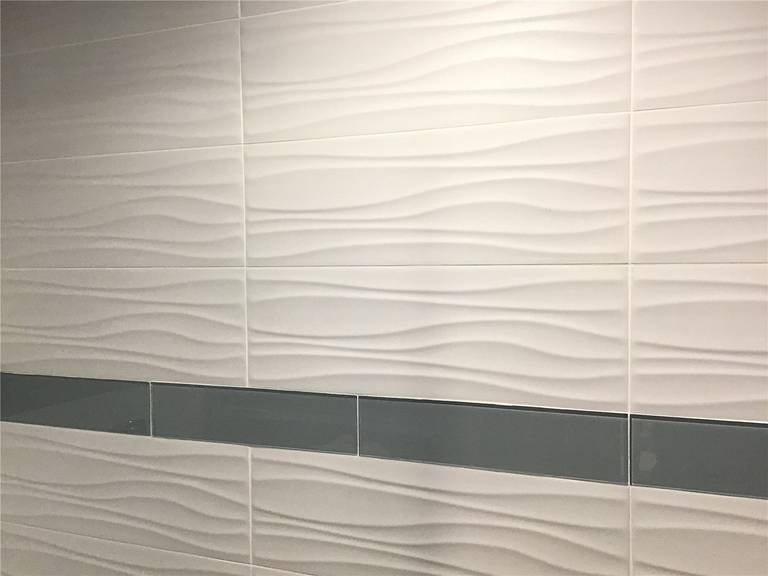 This Richmond Hill basement renovation features a modern bathroom wall design using textured 3D wave tiles combined with a sleek horizontal accent strip. The neutral color palette enhances the space with a clean and contemporary look, making it ideal for functional and stylish basement bathrooms. Perfect example of high-quality basement finishing in Richmond Hill.