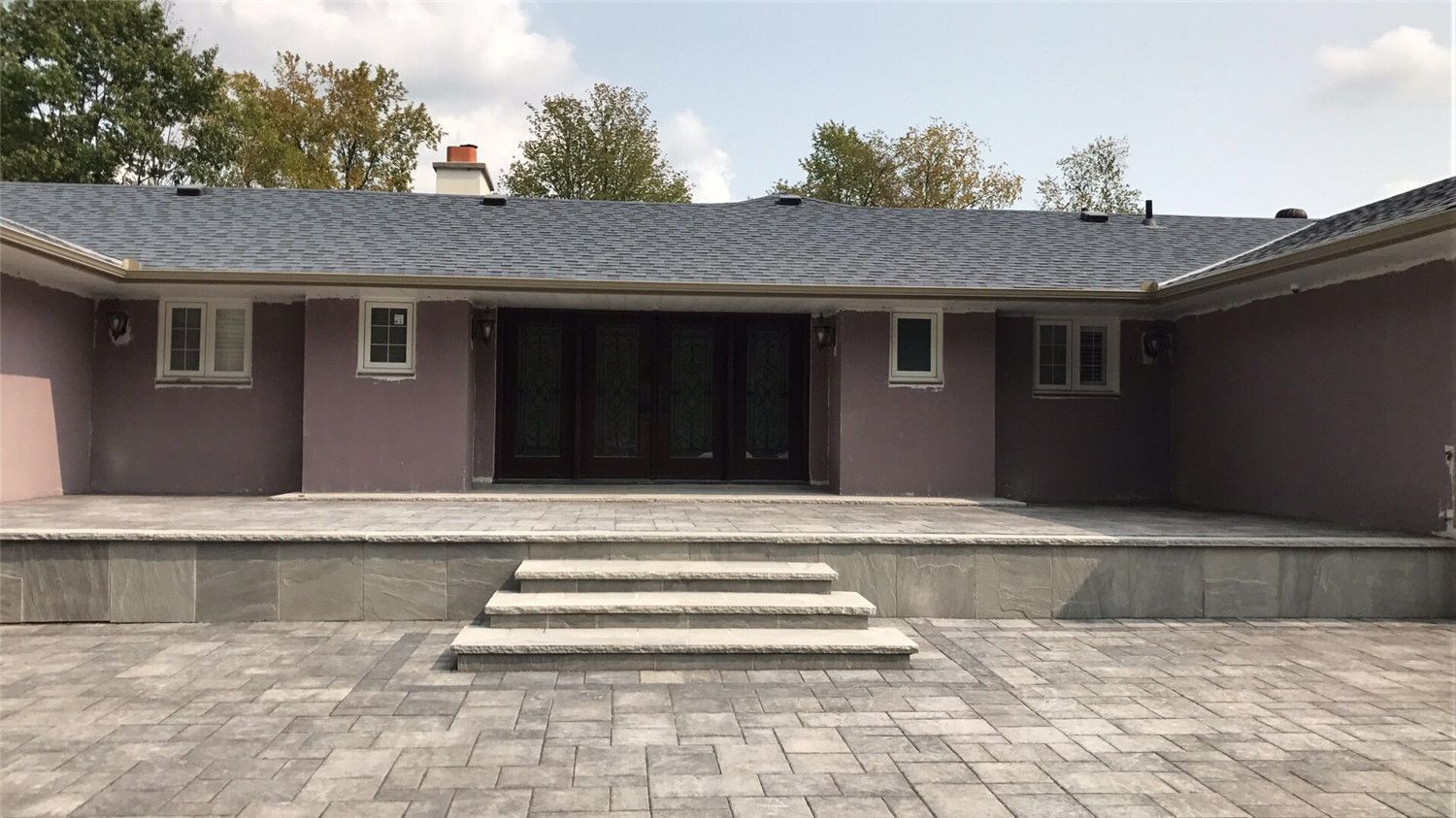 Professional Toronto backyard landscaping project featuring large interlocking patio stones, elevated deck platform, and modern stone steps leading to the garden area. The design creates a clean, functional outdoor living space that enhances both usability and visual appeal for the home.