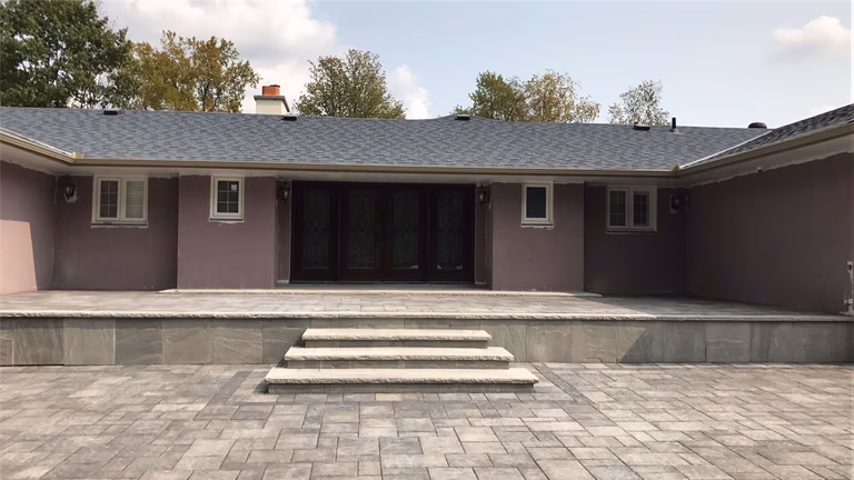 Professional Toronto backyard landscaping project featuring large interlocking patio stones, elevated deck platform, and modern stone steps leading to the garden area. The design creates a clean, functional outdoor living space that enhances both usability and visual appeal for the home.