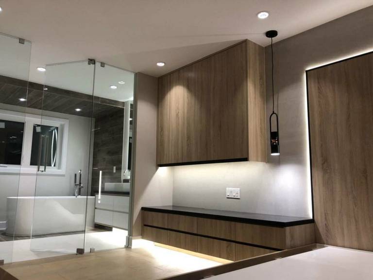 Stylish Markham home renovation featuring custom built-in cabinetry, floating storage, and warm wood panel finishes with integrated LED lighting. The space is enhanced by sleek glass partitions connecting the bedroom and luxury bathroom, creating a seamless, contemporary layout that balances functionality, comfort, and modern interior elegance.