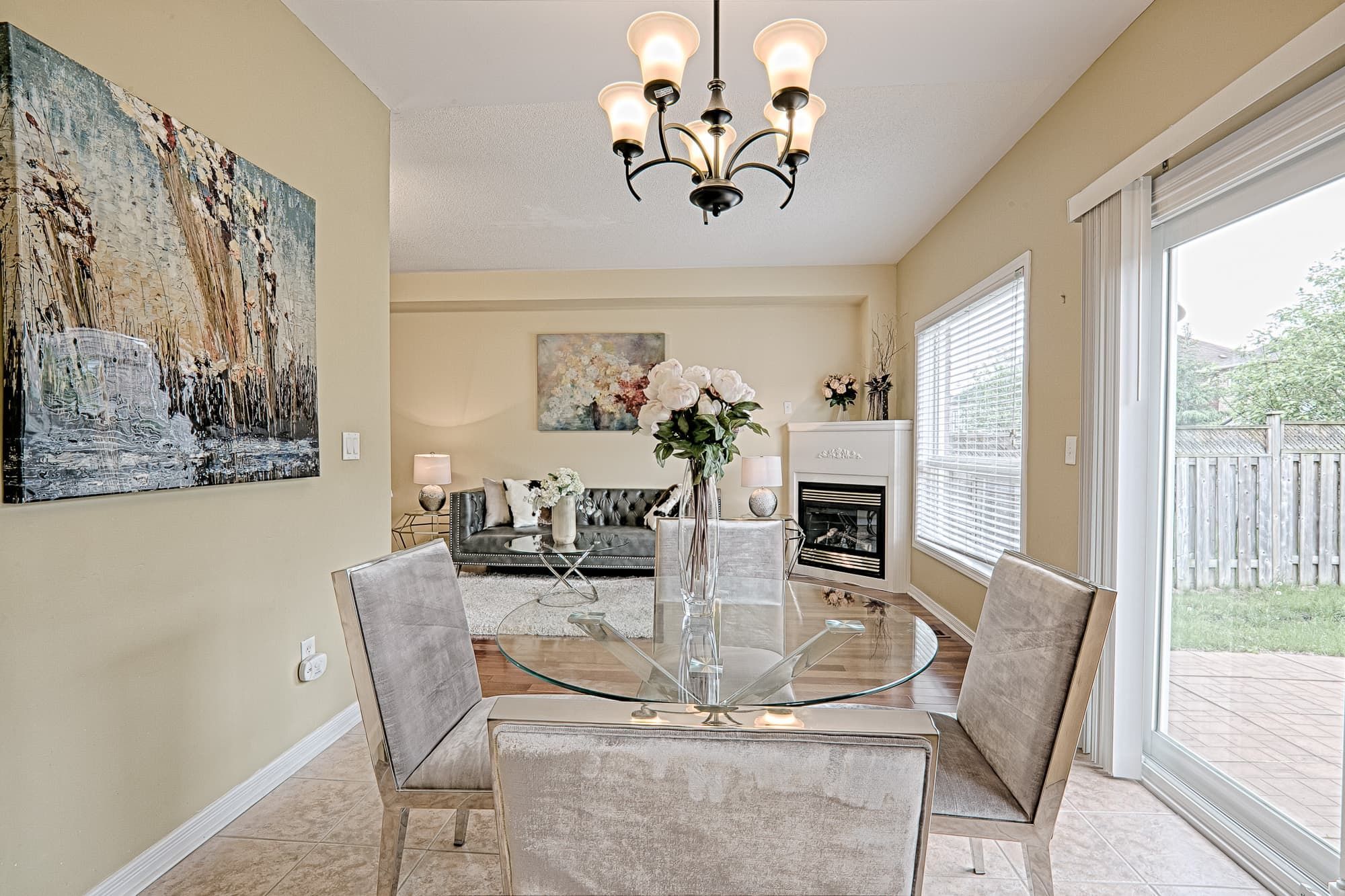 This open dining and living area reflects a simple and lovely interior design with an airy layout, soft neutral tones, and abundant natural light. The glass dining table and upholstered chairs create a light visual flow, while the connected living space enhances openness and functionality. Large windows and patio doors bring in natural light, making the space bright, comfortable, and ideal for everyday family living and entertaining.