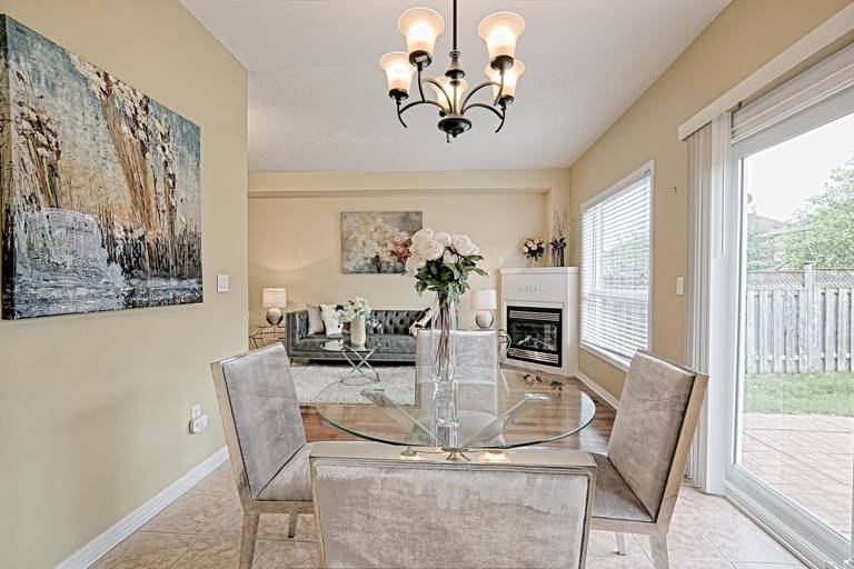 This open dining and living area reflects a simple and lovely interior design with an airy layout, soft neutral tones, and abundant natural light. The glass dining table and upholstered chairs create a light visual flow, while the connected living space enhances openness and functionality. Large windows and patio doors bring in natural light, making the space bright, comfortable, and ideal for everyday family living and entertaining.