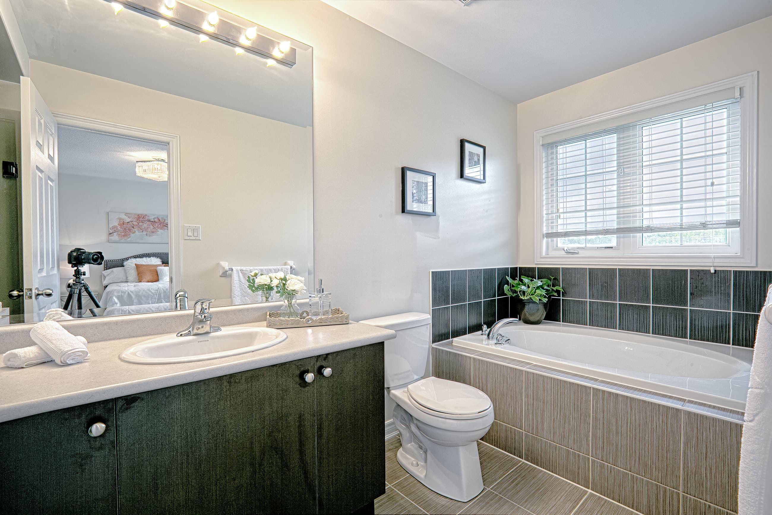This modern bathroom renovation features a clean vanity with a durable countertop, large wall mirror, and updated lighting that enhances brightness and visual space. The bathtub area is finished with contemporary tile detailing that adds texture while maintaining a neutral, cohesive palette. Designed for both everyday functionality and long-term durability, this bathroom upgrade reflects the high standards of a professional Toronto renovation company specializing in complete residential interior transformations.