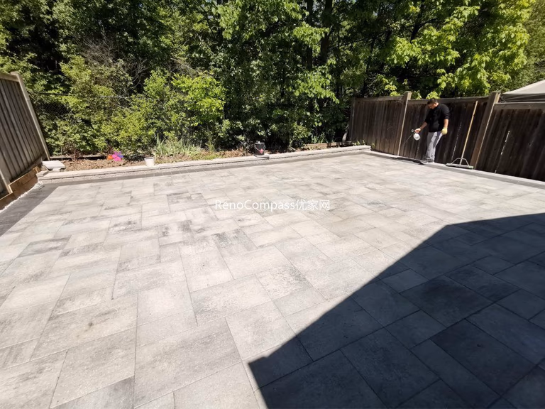 Modern Mississauga backyard patio featuring interlocking stone flooring, raised retaining wall, and landscaped garden beds, creating a functional and elegant outdoor living space.