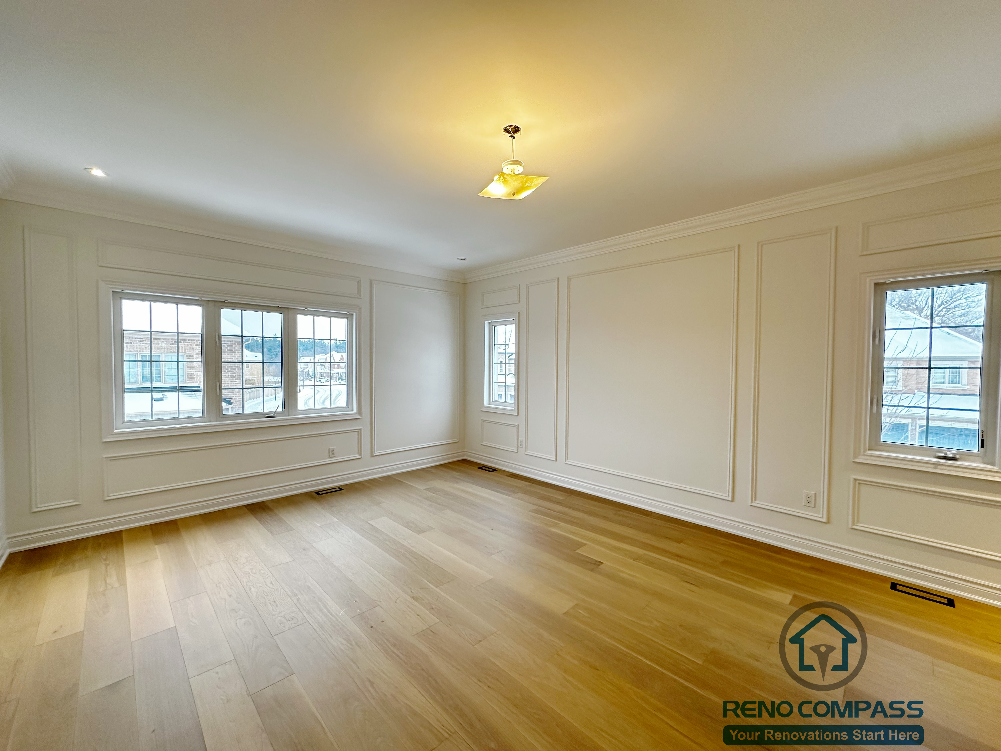 Bright room completed as part of a Vaughan interior renovation, featuring custom wall panel detailing, crown moulding, wide-plank hardwood flooring, and large windows that provide abundant natural light. The clean finishes and balanced layout reflect the craftsmanship of a professional Toronto renovation company.