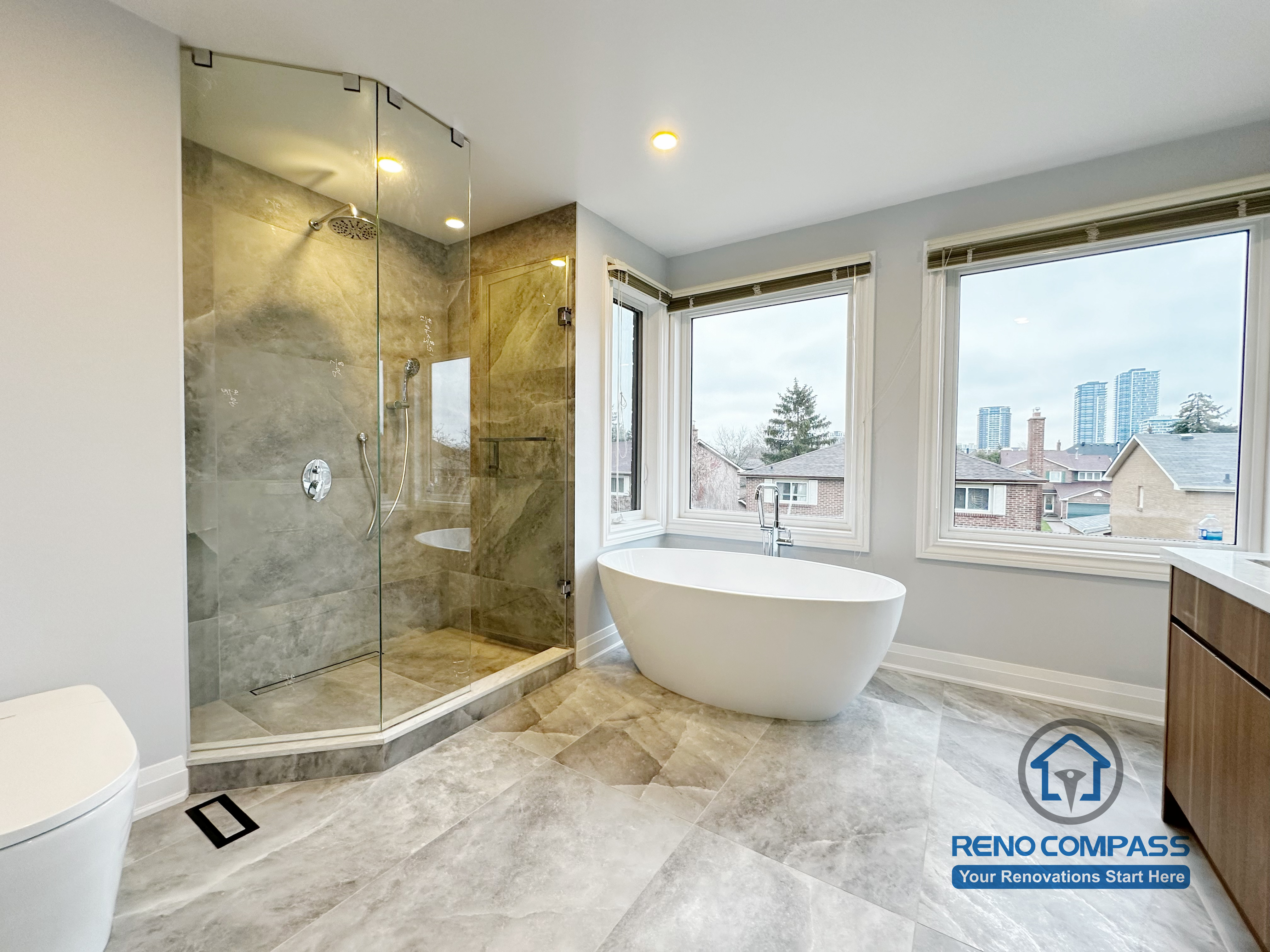Bathroom renovation in Markham featuring a freestanding soaking tub, frameless glass shower, and large-format tile flooring. Expansive windows enhance natural light, creating a bright, spa-inspired bathroom with a clean and modern layout.