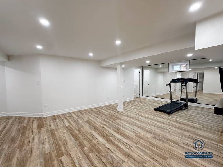 This image showcases a completed basement renovation in Pickering, featuring an open-concept layout designed for flexible everyday use. The space combines a functional kitchenette, open living area, and exercise zone, supported by consistent flooring and recessed lighting throughout. Structural columns are carefully integrated into the layout to maintain openness while preserving necessary support. Neutral finishes and clean ceiling lines enhance brightness and visual continuity, allowing the basement to function comfortably as an extension of the main living area.
Location: Pickering · Toronto Contractor: Reno Compass