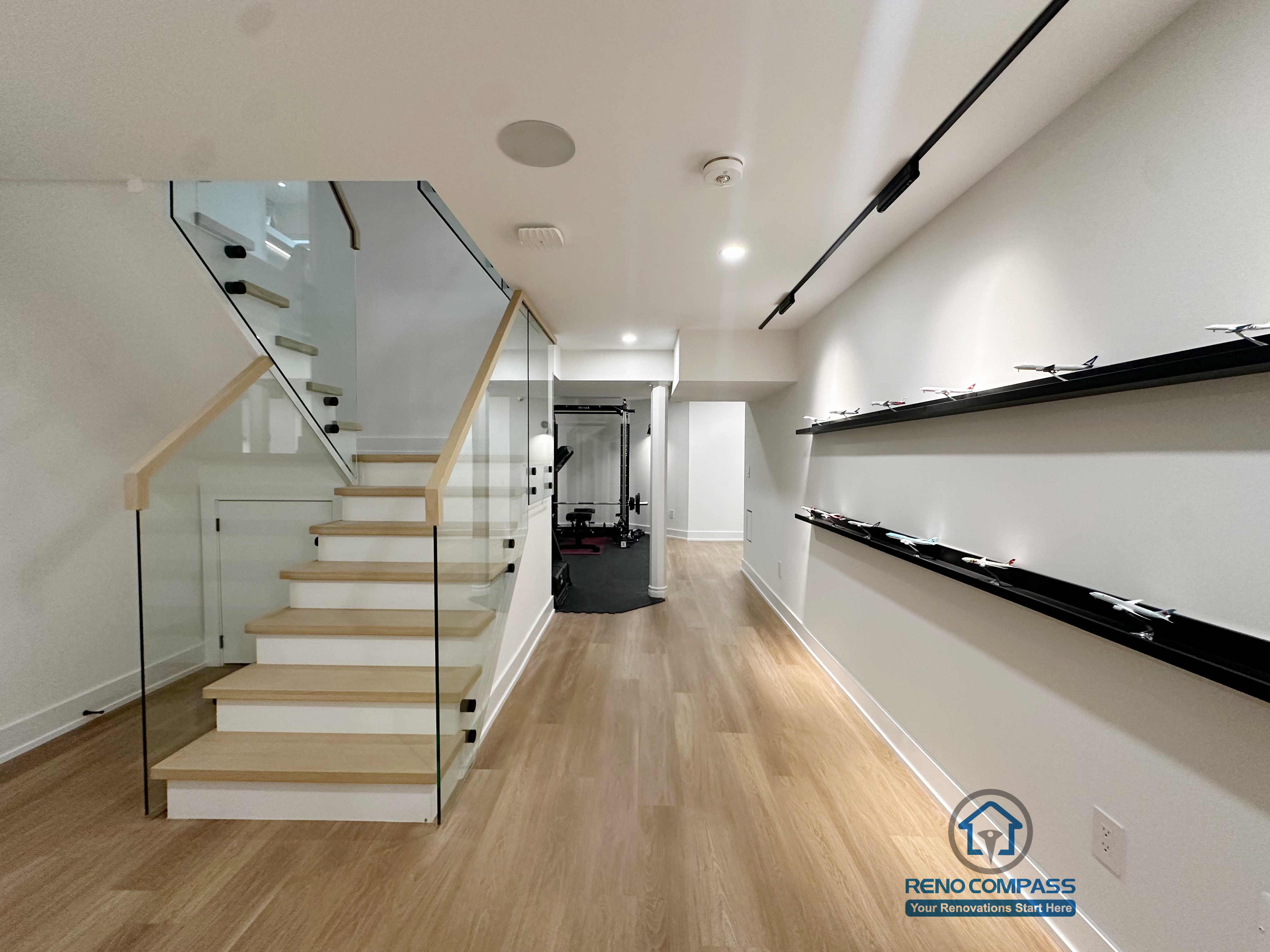 Under-stair space beneath a floating steel staircase with glass railing and wood treads in a Markham residential renovation .This view highlights the thoughtful use of space beneath the floating steel staircase. By combining tempered glass panels with solid wood treads, the design maintains visual openness and smooth circulation at the main-floor level. The area beneath the stairs remains bright and unobstructed, enhancing both spatial flow and everyday functionality within the home.