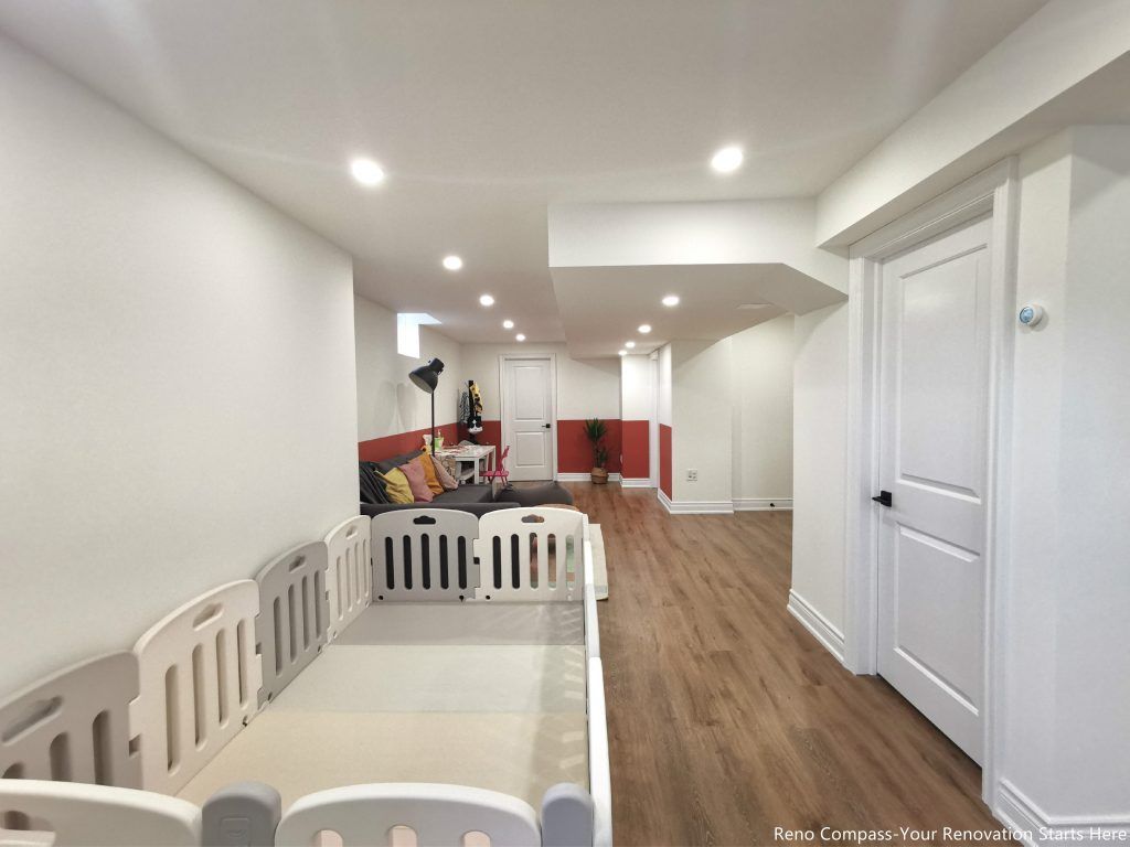 This image showcases a fully renovated open concept basement in Vaughan, featuring a spacious layout designed for multiple functions including family living, children’s play, and entertainment. Upgraded wood flooring runs throughout the space, creating visual continuity and durability for everyday use. Recessed ceiling lighting, structural column integration, and a well-planned ceiling layout enhance brightness and comfort while maintaining clean lines. The combination of open circulation and defined activity zones reflects thoughtful space planning and craftsmanship delivered by a professional Toronto renovation company specializing in livable basement renovations.
