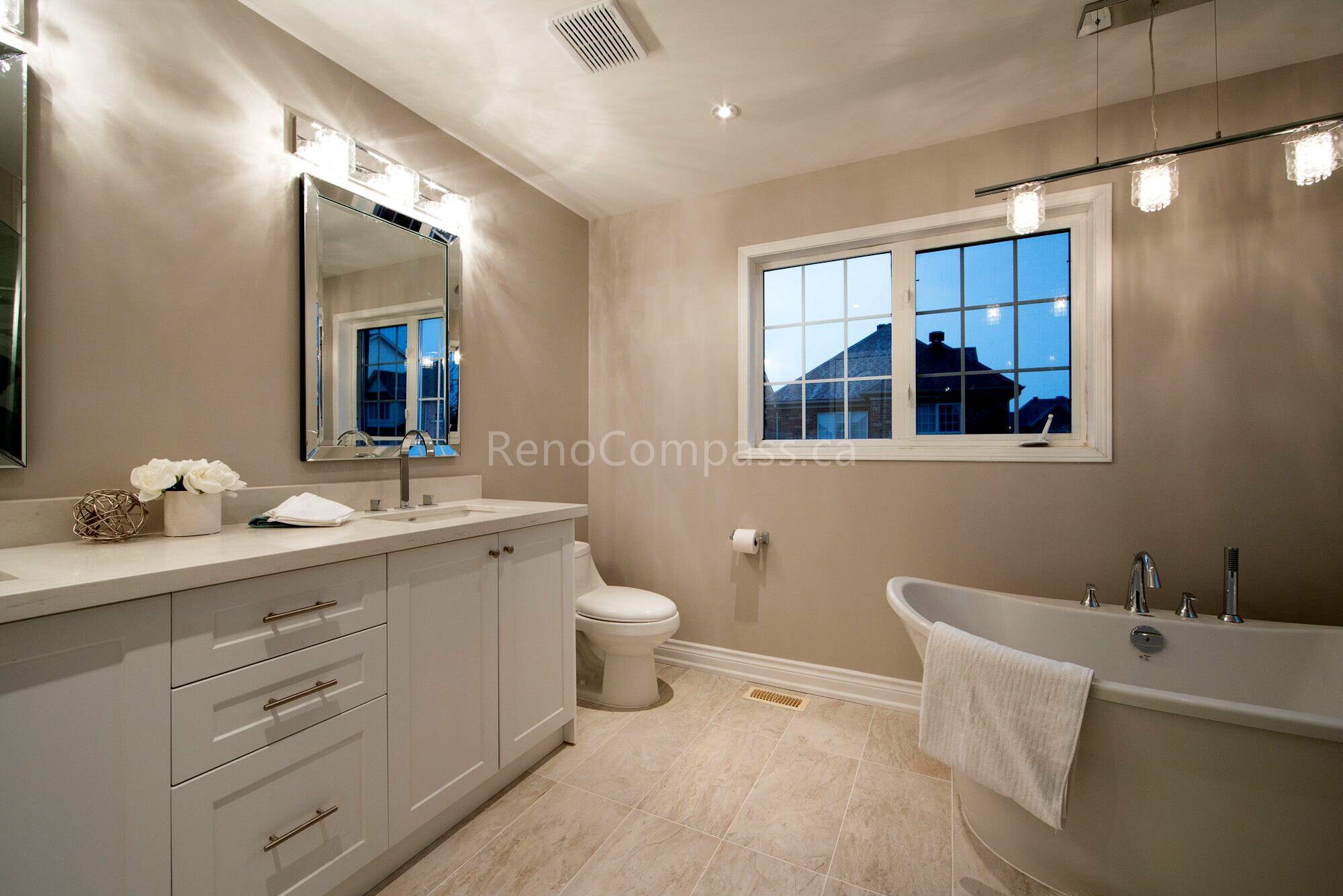 A bright master bathroom interior renovation in Toronto featuring a custom vanity with ample storage, freestanding bathtub, modern lighting, and large window for natural light. The design focuses on comfort, functionality, and timeless finishes, showcasing professional Toronto interior renovation and interior design craftsmanship.
