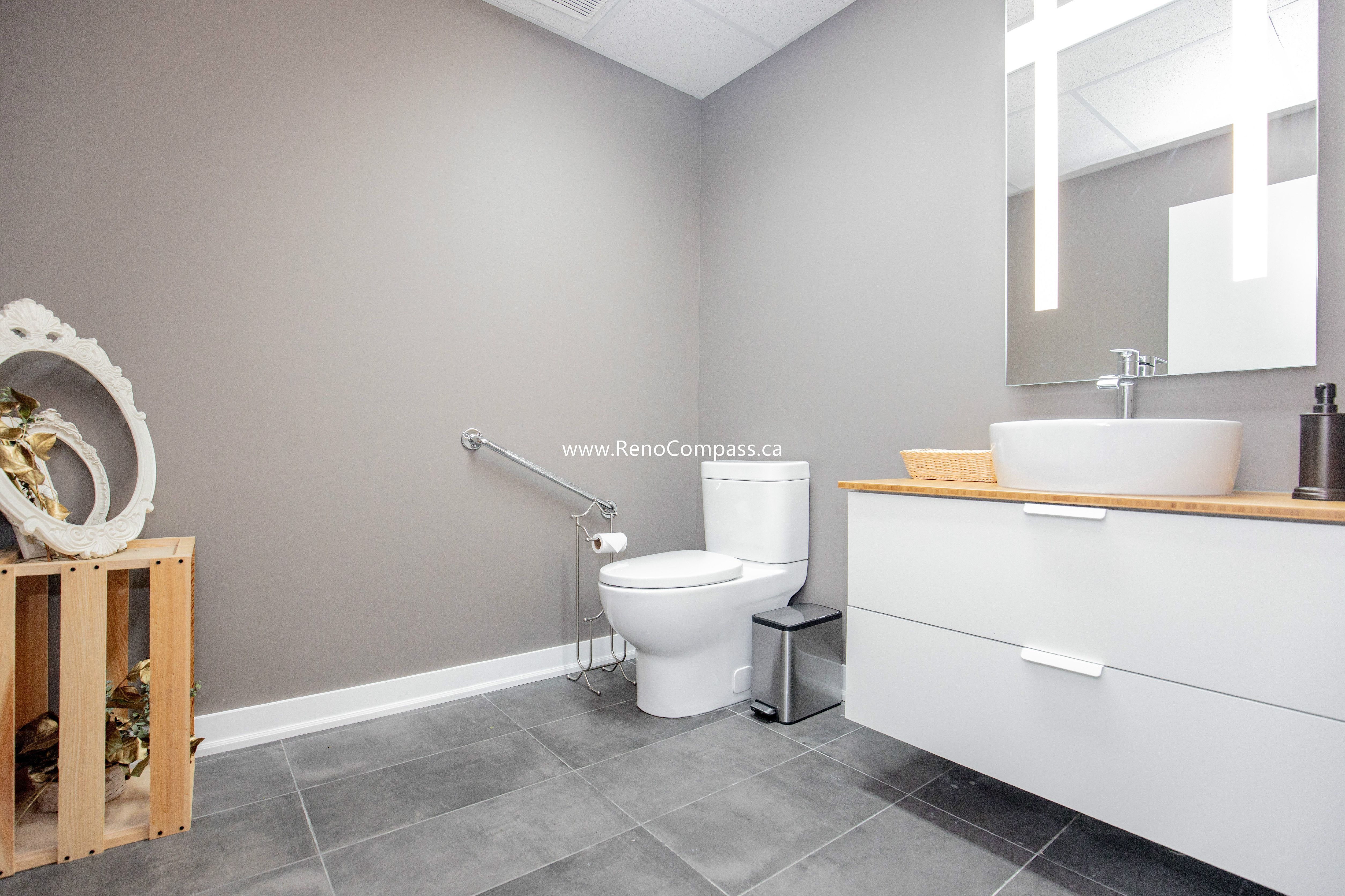 A professional commercial bathroom renovation featuring a modern floating vanity with a vessel sink, grey porcelain tile flooring, and ADA-compliant grab bars. Designed for comfort and style at The Singing School in Richmond Hill.