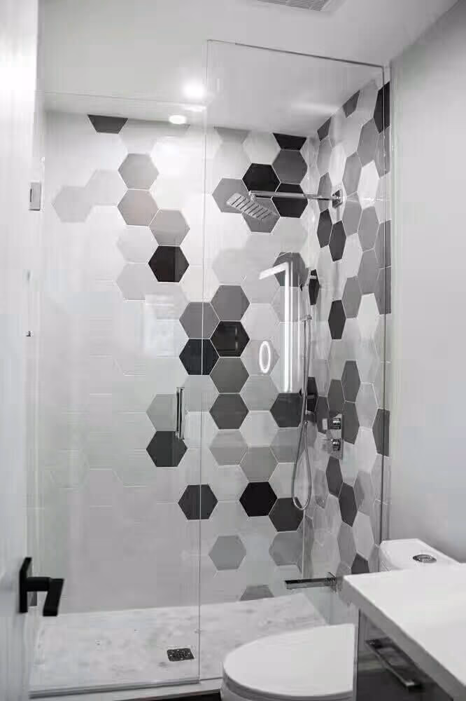 This Markham interior renovation features a modern bathroom upgrade with a custom glass-enclosed shower and striking hexagon tile accent wall. The neutral grey and white tile palette adds visual depth while maintaining a clean, contemporary look. Matte black fixtures, a frameless glass door, and a compact floating vanity maximize functionality in a limited space. Designed for durability and everyday comfort, this bathroom renovation reflects the quality craftsmanship of a professional Toronto renovation contractor.