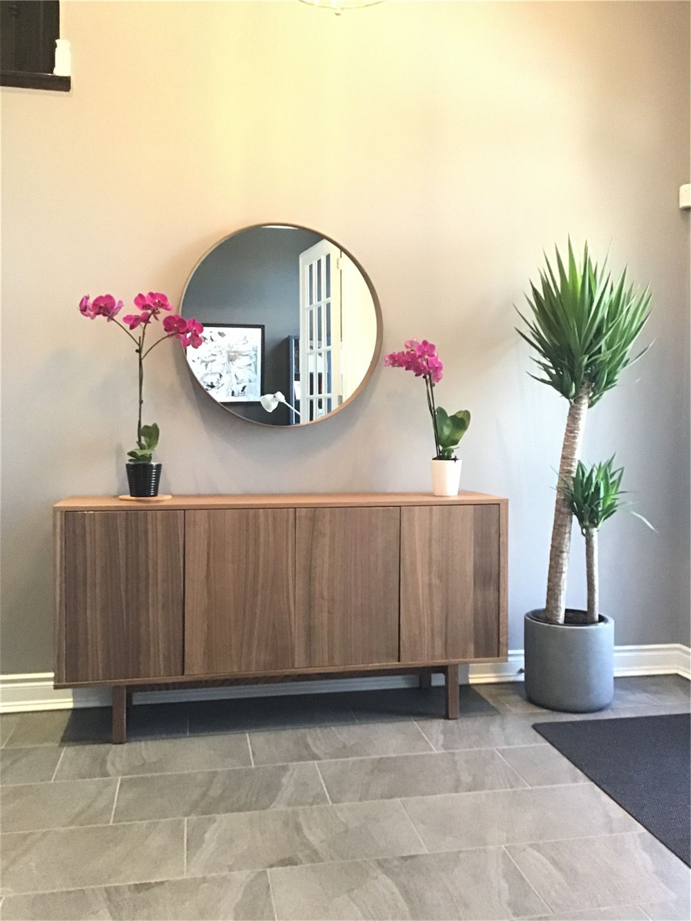 This Markham full home renovation features a clean and welcoming entryway with a modern wood console table, round wall mirror, and minimalist decor accents. The neutral tones, indoor plants, and tiled flooring create a balanced and inviting first impression. Completed by a professional Toronto Renovation Company, this space reflects thoughtful design and everyday functionality.