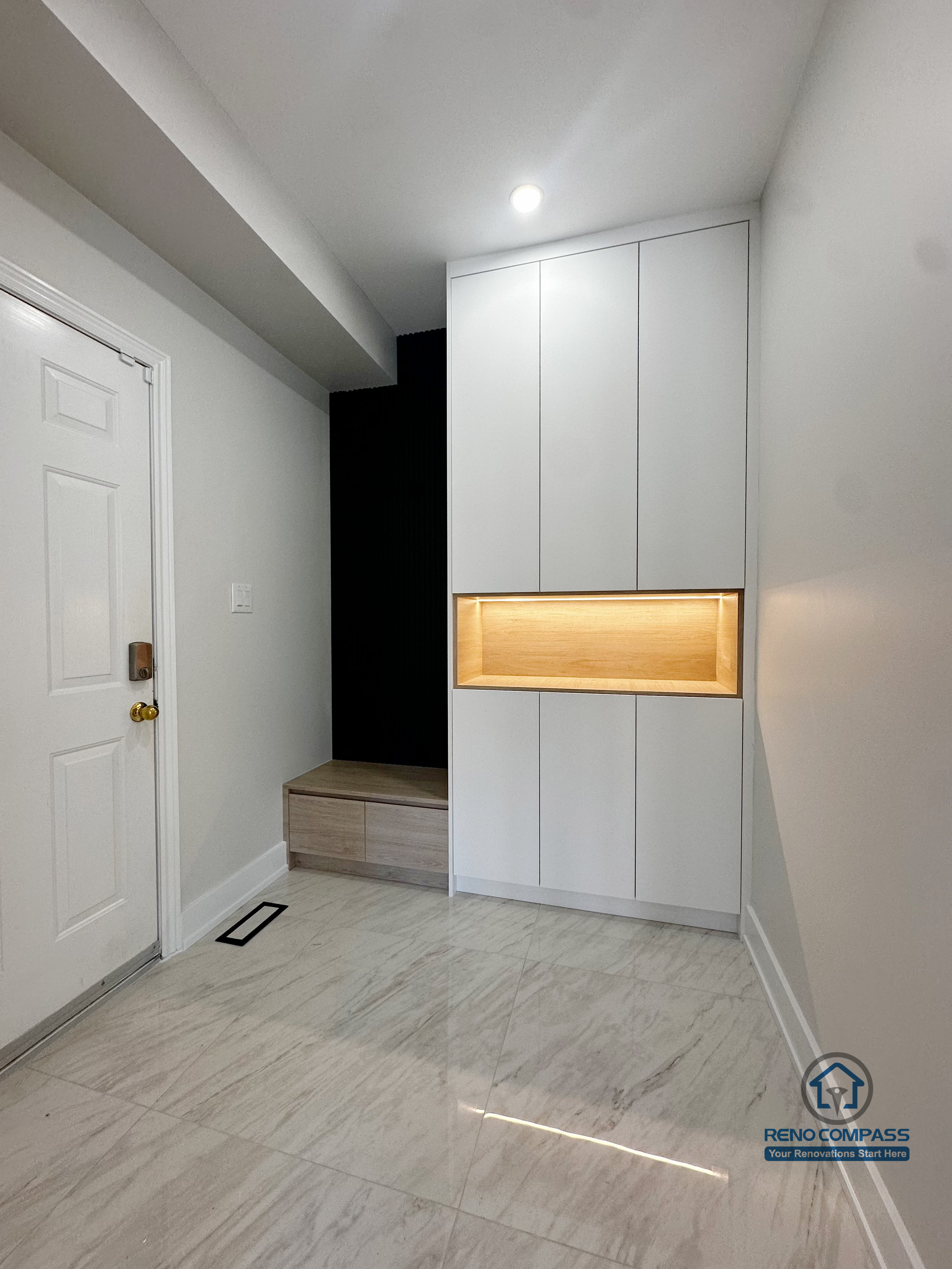 This Markham interior renovation features a custom-built entryway storage system designed to improve daily functionality while maintaining a clean, modern aesthetic. Full-height cabinetry provides concealed storage, while the integrated wood-accent niche with warm backlighting adds visual focus and practical surface space. The recessed bench area creates a convenient transition zone for shoes and outerwear, making the entry both organized and welcoming. Neutral finishes and integrated lighting ensure the space feels bright, efficient, and well-balanced.