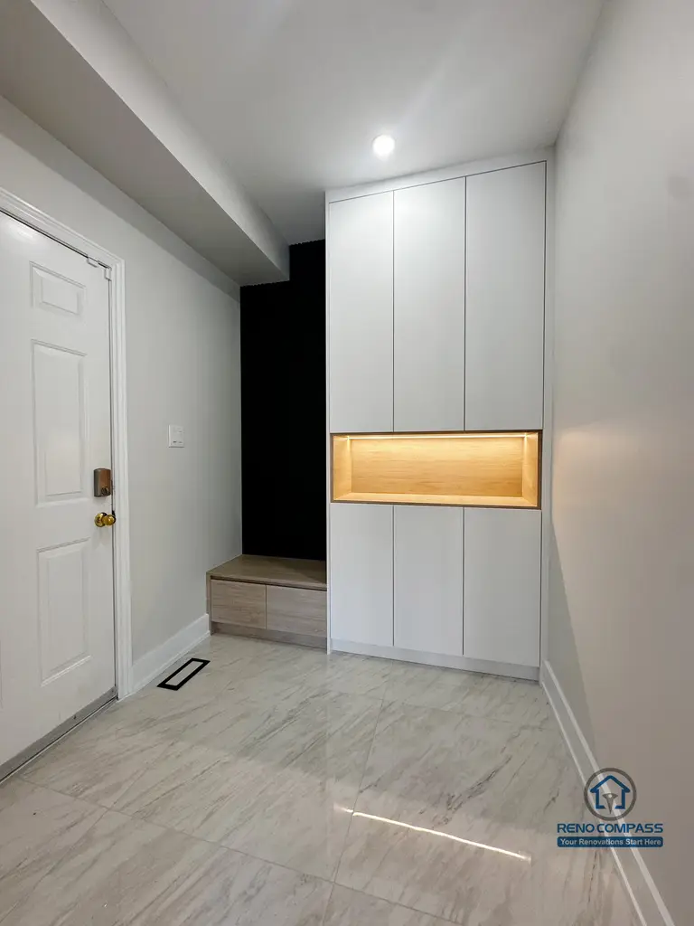 This Markham interior renovation features a custom-built entryway storage system designed to improve daily functionality while maintaining a clean, modern aesthetic. Full-height cabinetry provides concealed storage, while the integrated wood-accent niche with warm backlighting adds visual focus and practical surface space. The recessed bench area creates a convenient transition zone for shoes and outerwear, making the entry both organized and welcoming. Neutral finishes and integrated lighting ensure the space feels bright, efficient, and well-balanced.