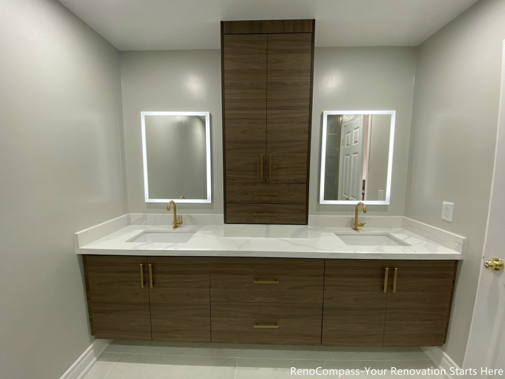 This Oakville master bathroom renovation showcases a modern double-sink vanity with custom wood cabinetry, quartz countertop, and elegant gold fixtures. The design features large-format floor tiles, LED backlit mirrors, and a sleek glass shower, creating a bright and luxurious spa-like atmosphere. Completed by a professional Toronto renovation company, this bathroom upgrade focuses on functionality, storage, and contemporary style, enhancing both comfort and property value for the homeowner.