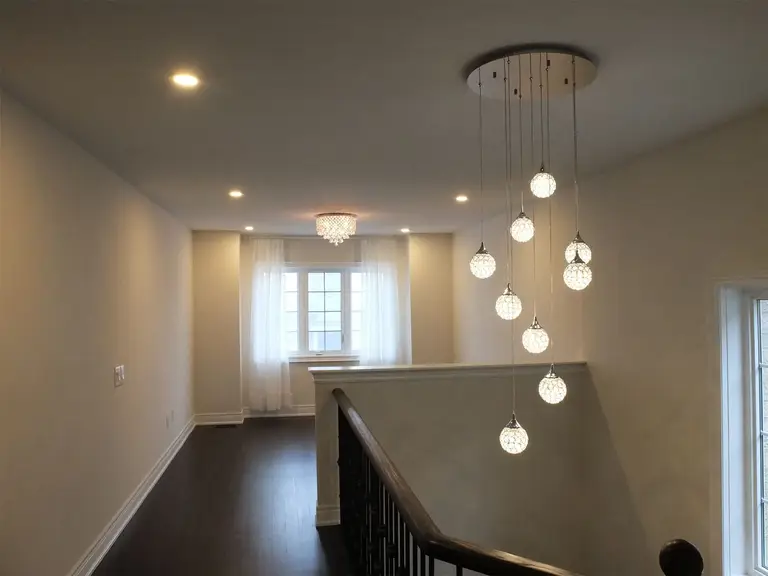 This Kleinburg interior renovation features a dramatic multi-pendant chandelier installed above the staircase, creating a striking focal point for the upper hallway. The cascading glass lights add elegance and depth to the open stairwell, while recessed pot lights provide balanced ambient lighting. Paired with dark hardwood flooring, neutral walls, and natural daylight from nearby windows, the space feels bright, modern, and architecturally refined.