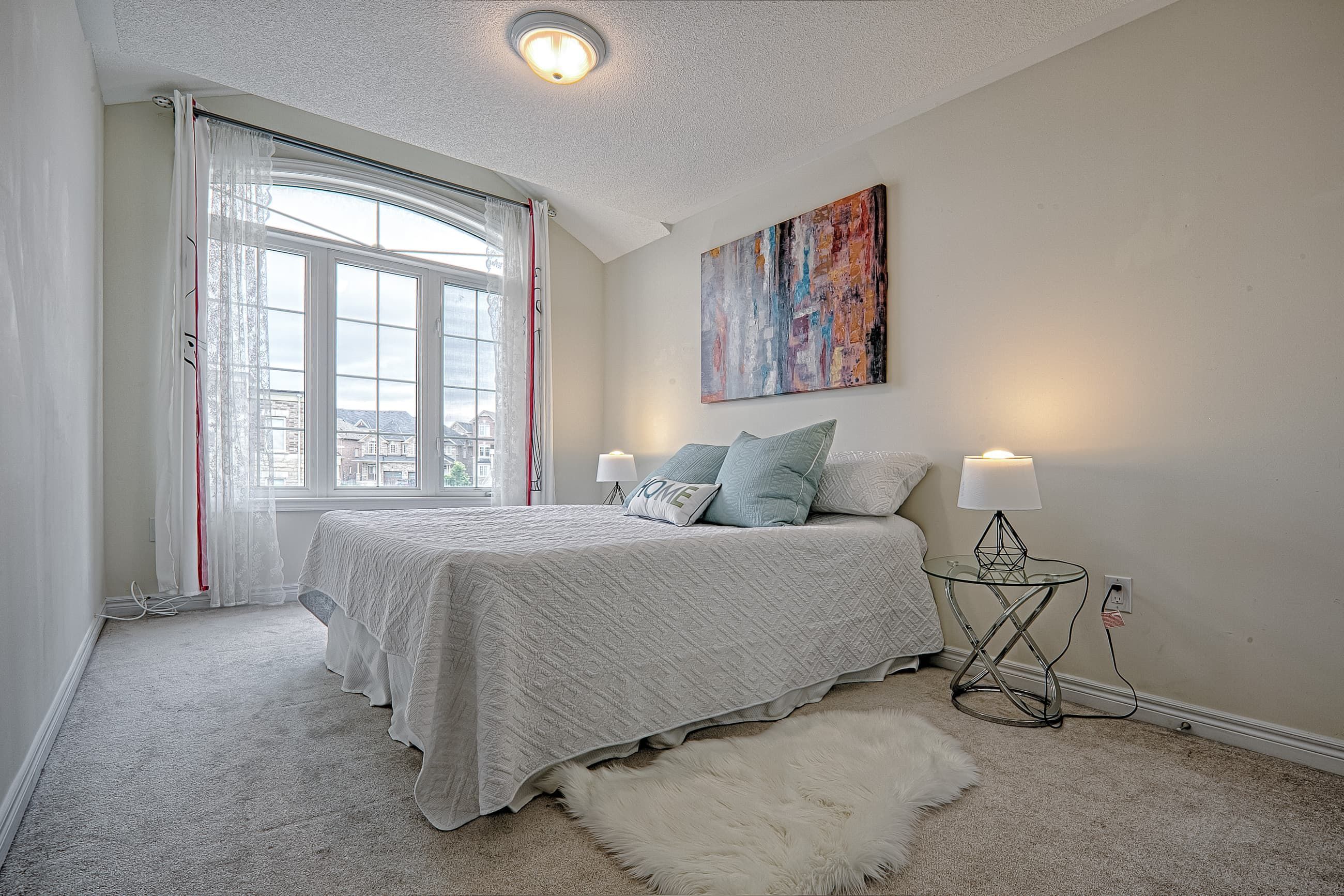 This modern master bedroom renovation showcases a calm and elegant design with soft neutral tones, plush carpeting, and large arched windows that bring in abundant natural light. The clean layout, cozy bedding, and contemporary bedside lighting create a relaxing and comfortable atmosphere ideal for everyday living. Completed by a professional Toronto renovation company, this bedroom upgrade highlights thoughtful space planning and refined interior finishes tailored for modern residential homes.
